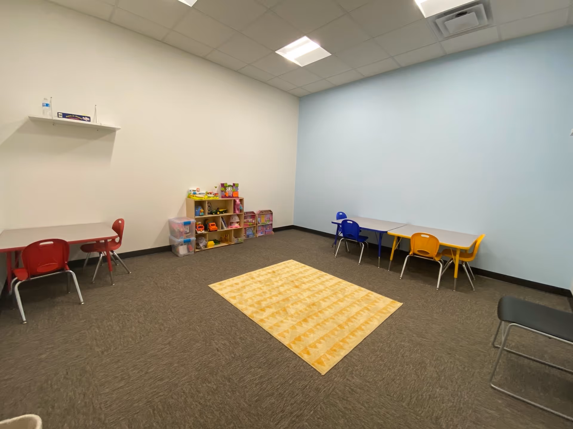 Bright playroom with small tables, colorful chairs, and toy shelves in a kid-friendly space.