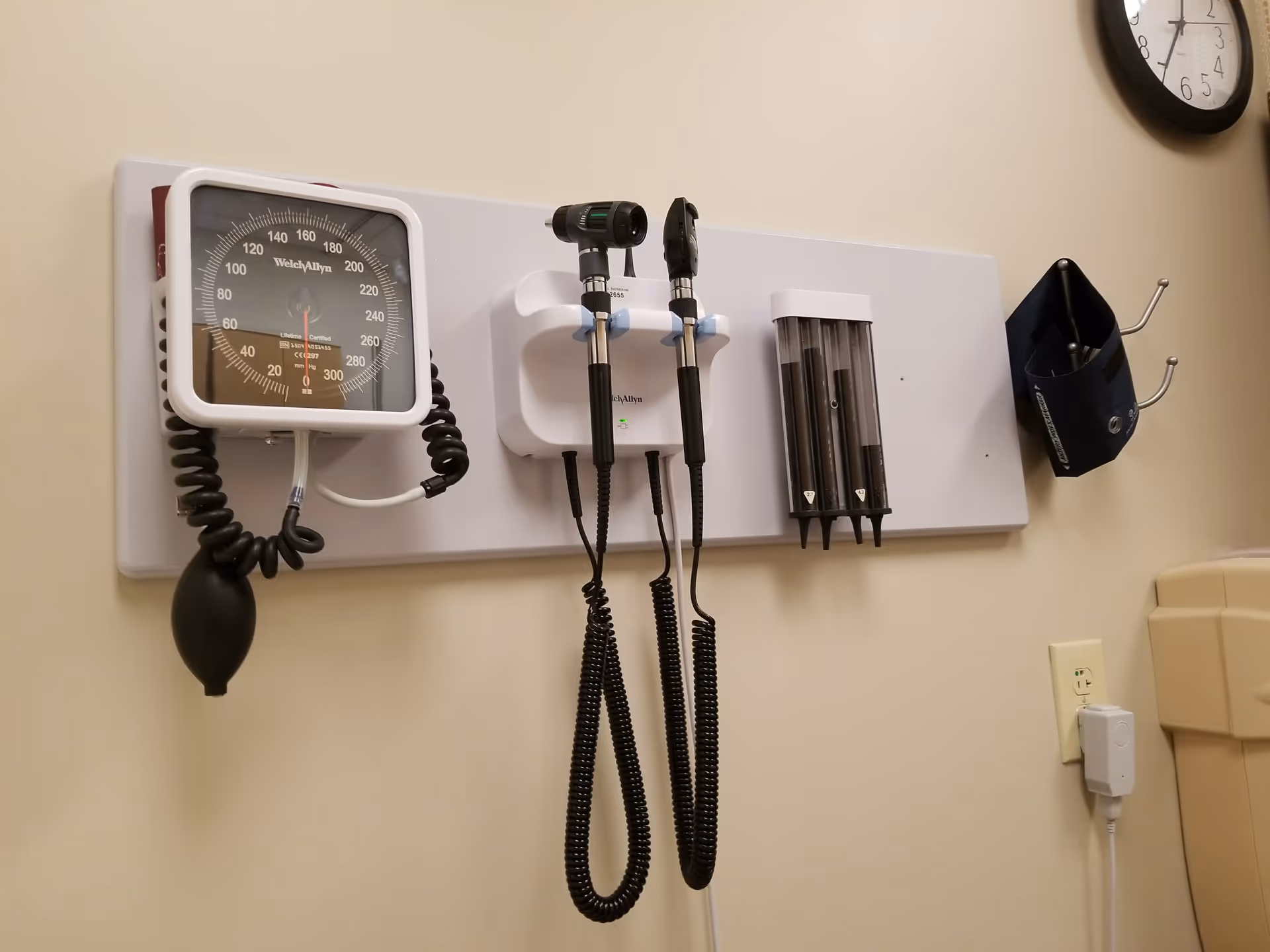 Wall-mounted medical devices in an examination room, including blood pressure gauge and scopes.