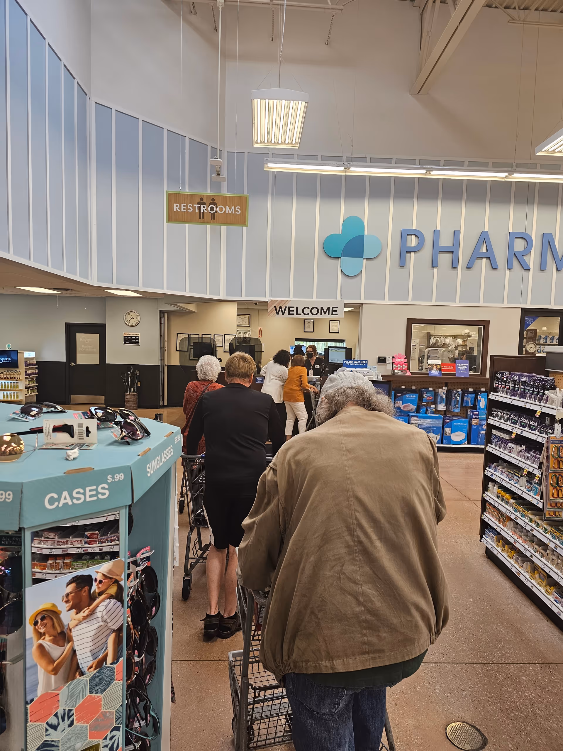 Inside a Kroger Pharmacy area with customers waiting in line near shelves.