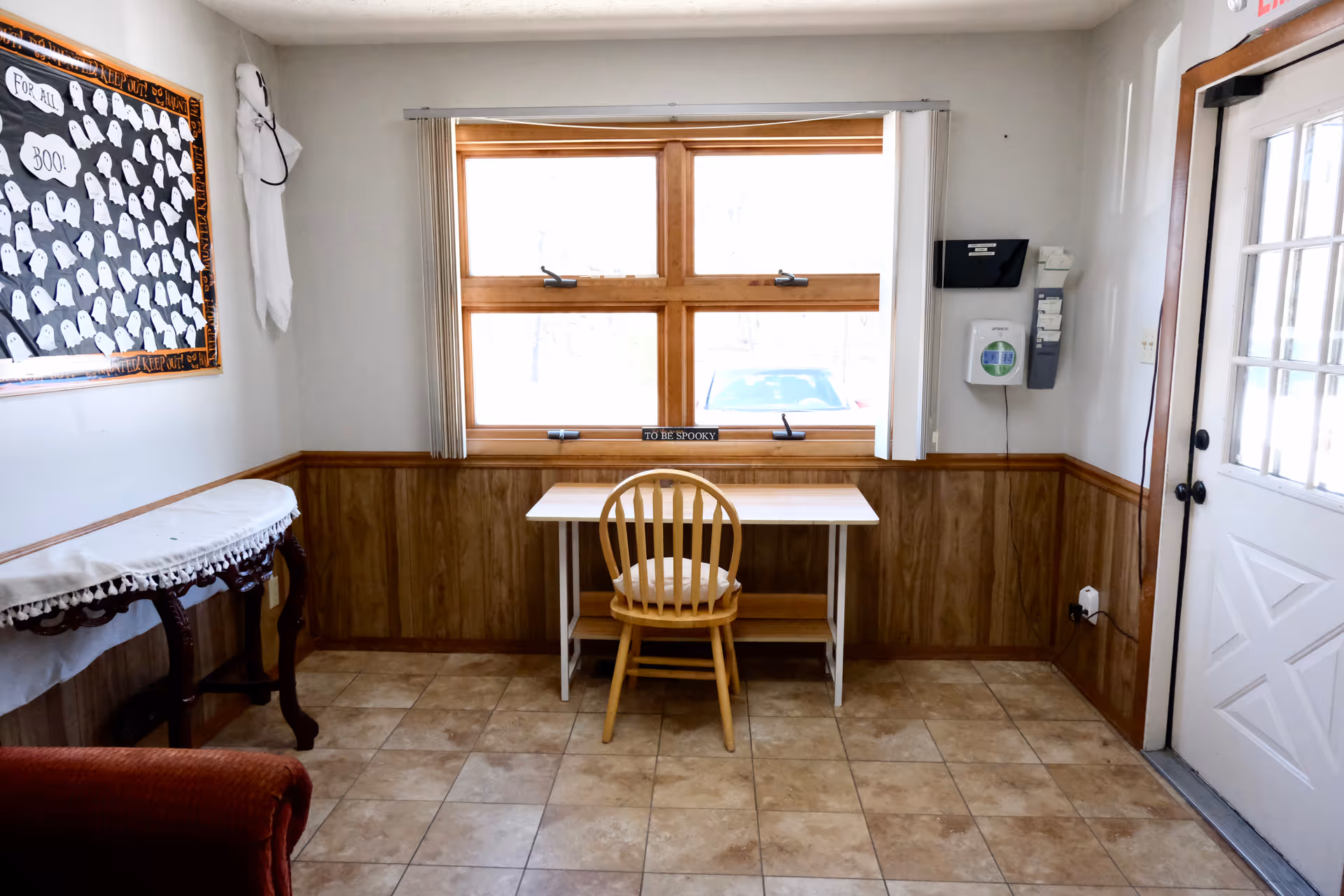 Small interior room with a desk by a window, wooden paneling, and a single chair.