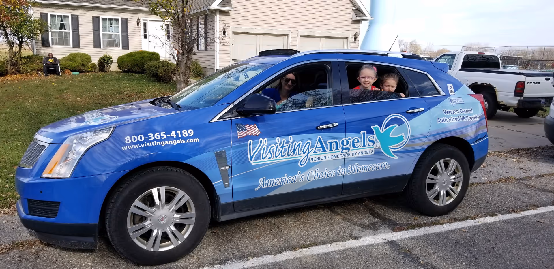 Blue Visiting Angels van parked roadside with smiling passengers visible through windows.