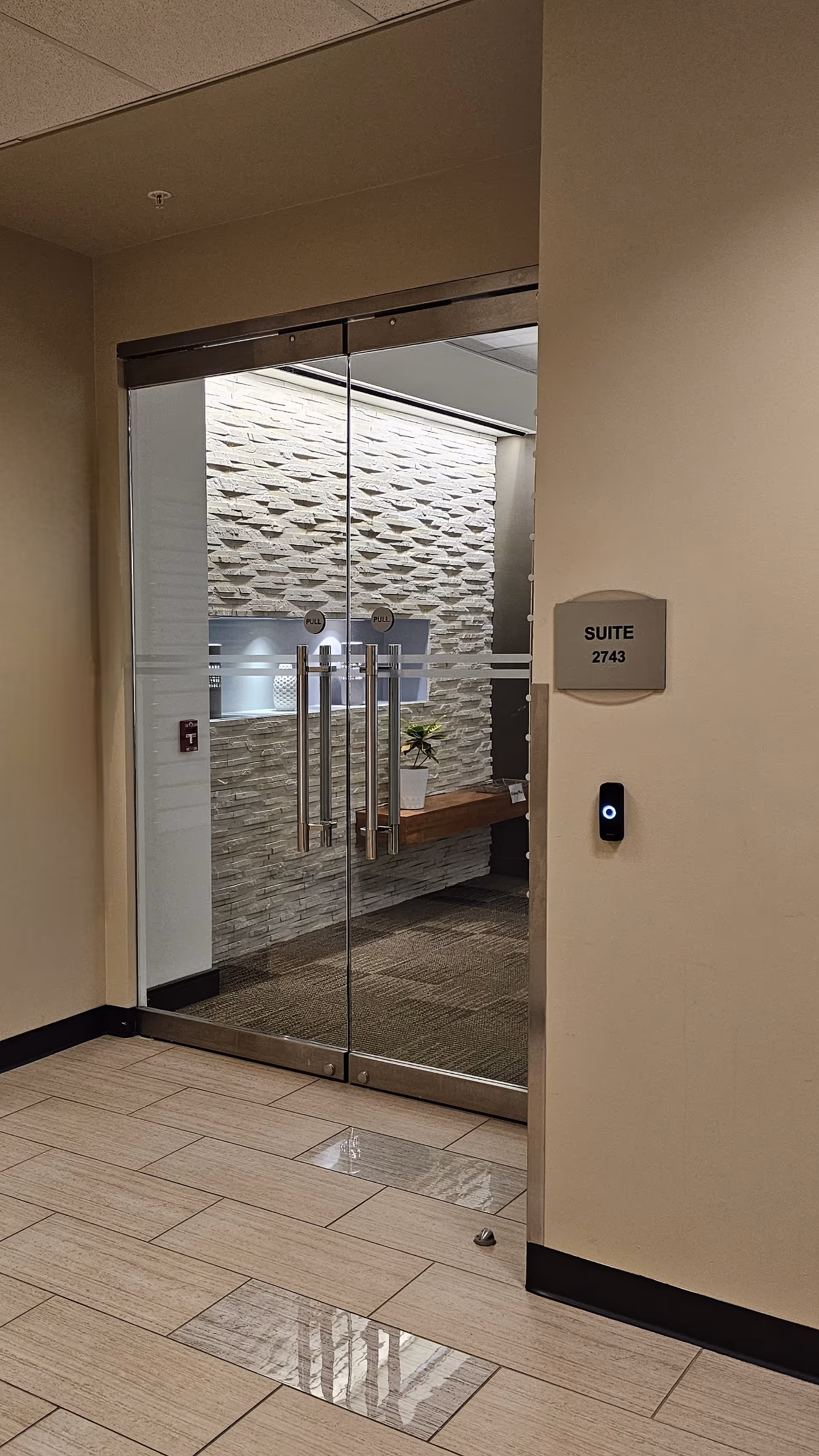 Interior hallway with glass doors to a suite and a stone accent wall.