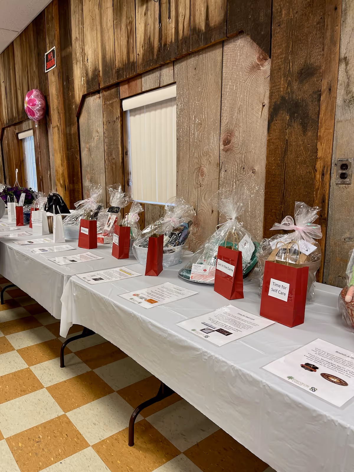Long table with gift baskets and papers along a rustic wood-paneled interior.
