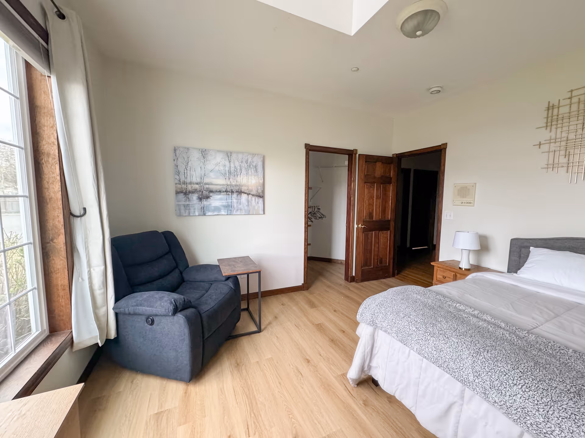 Bedroom in a senior living facility featuring a bed, recliner, window, and nightstand.