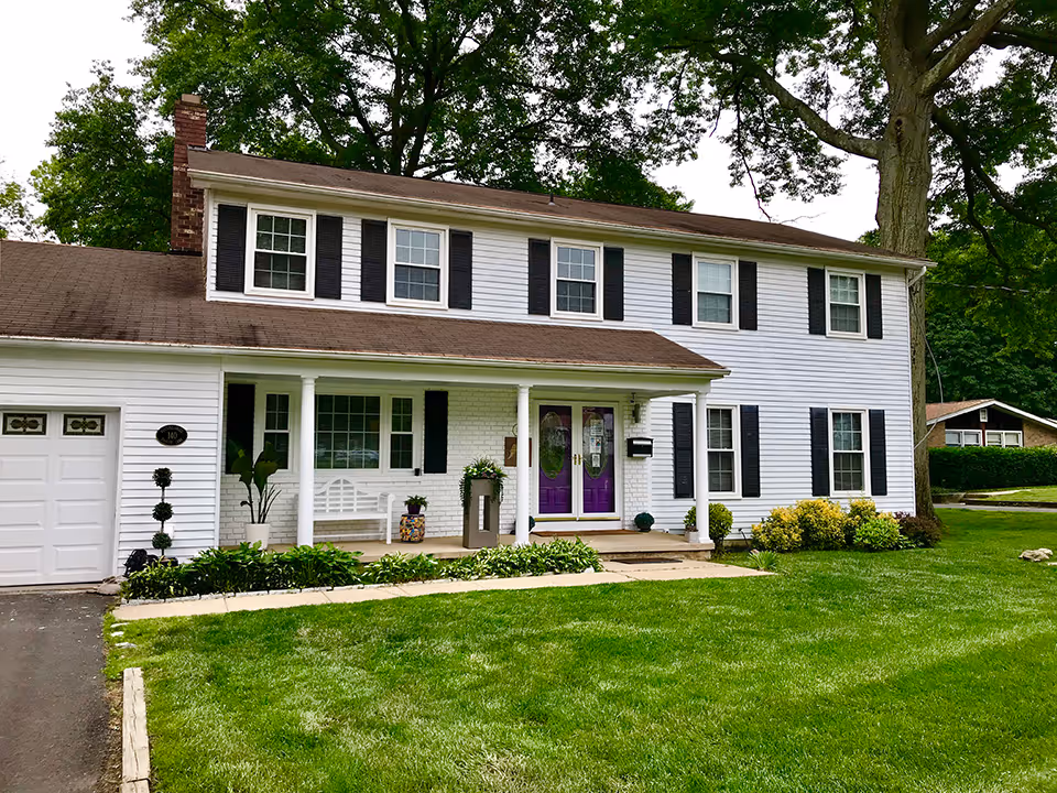 White two-story home with purple doors, columns, and a well-kept lawn