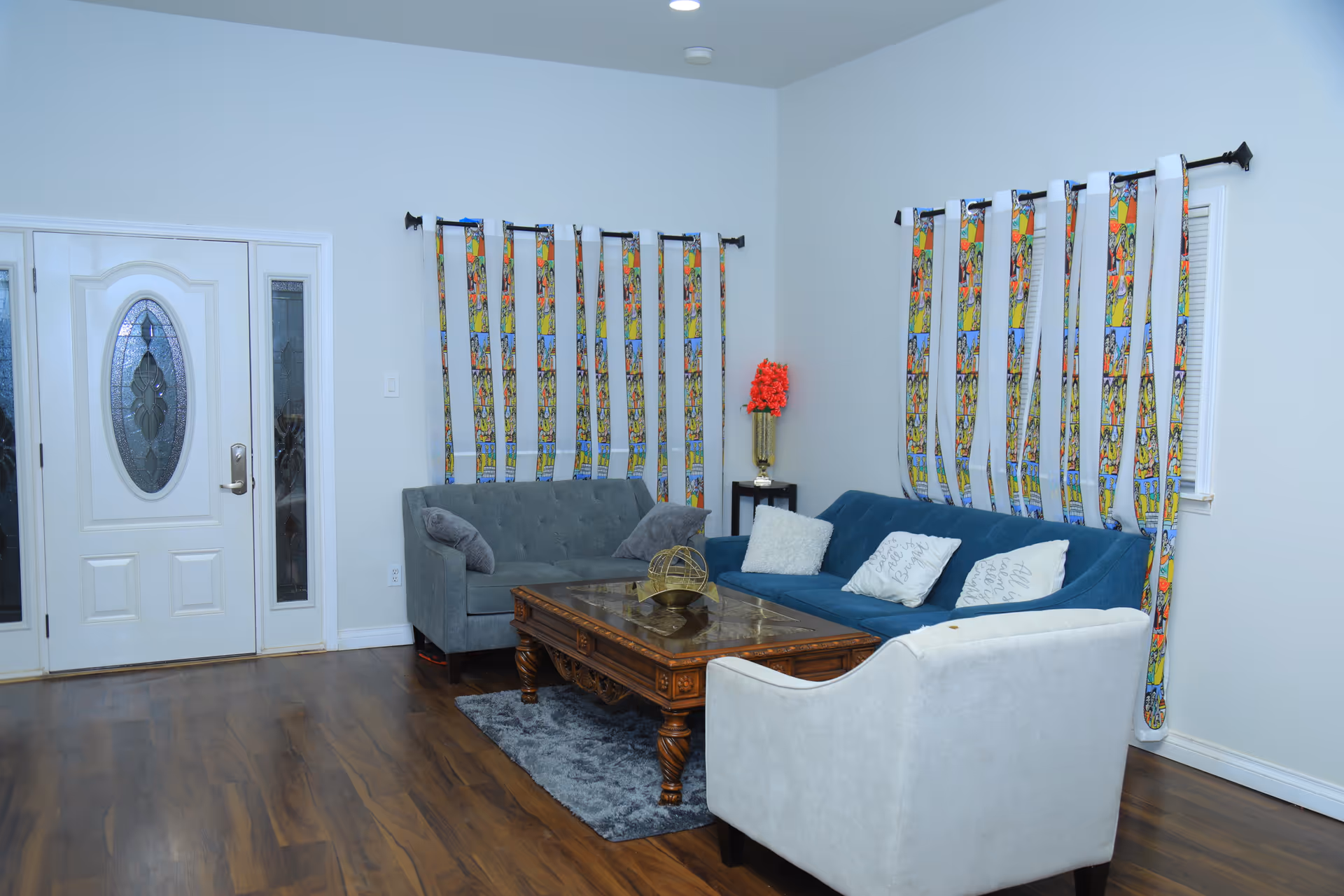 Bright living room with blue sofa, white armchair, wooden coffee table, and colorful patterned curtains.