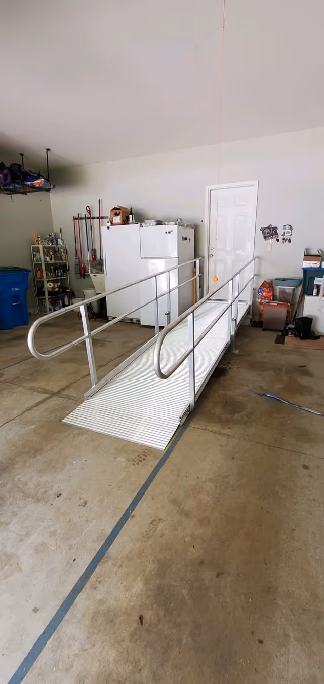 Indoor garage-like space with a metal wheelchair ramp leading to a white door.