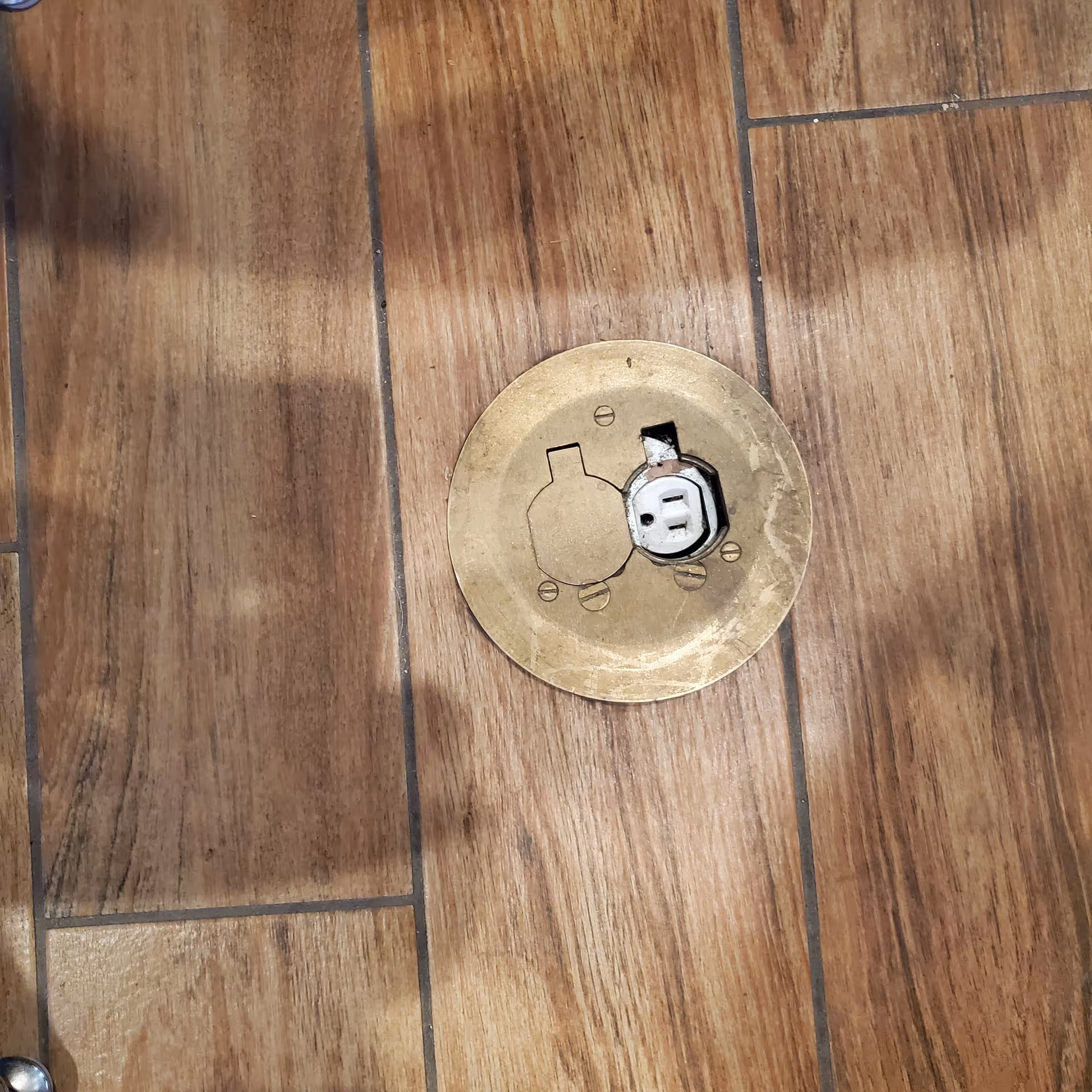 Close-up of a brass circular floor drain set in wood-look tile flooring.