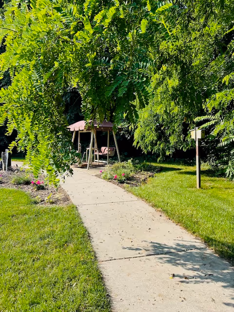 A shaded outdoor pathway with benches and a gazebo on a manicured lawn