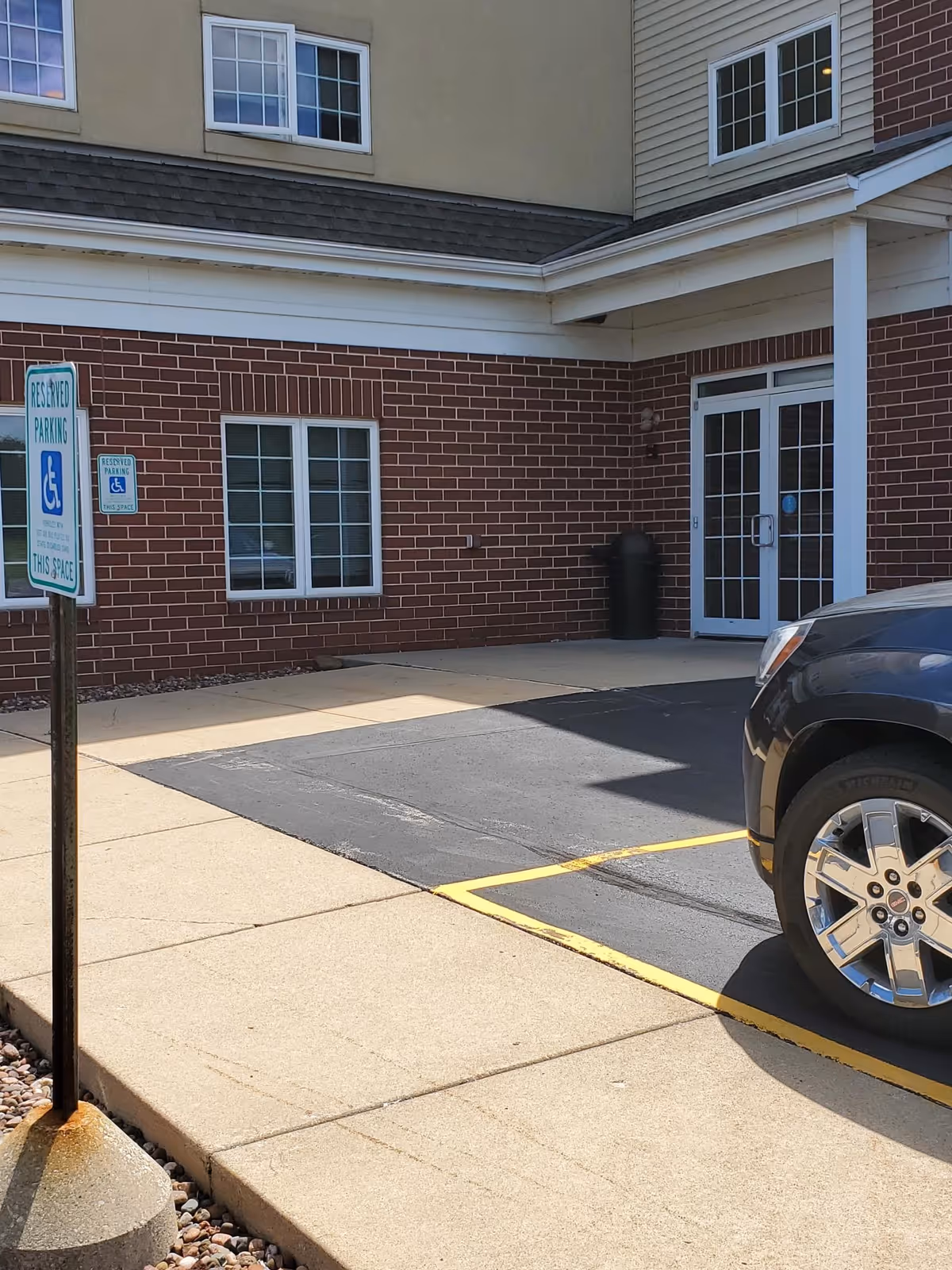 Exterior view of a brick facility entrance with reserved parking and a wheelchair sign.