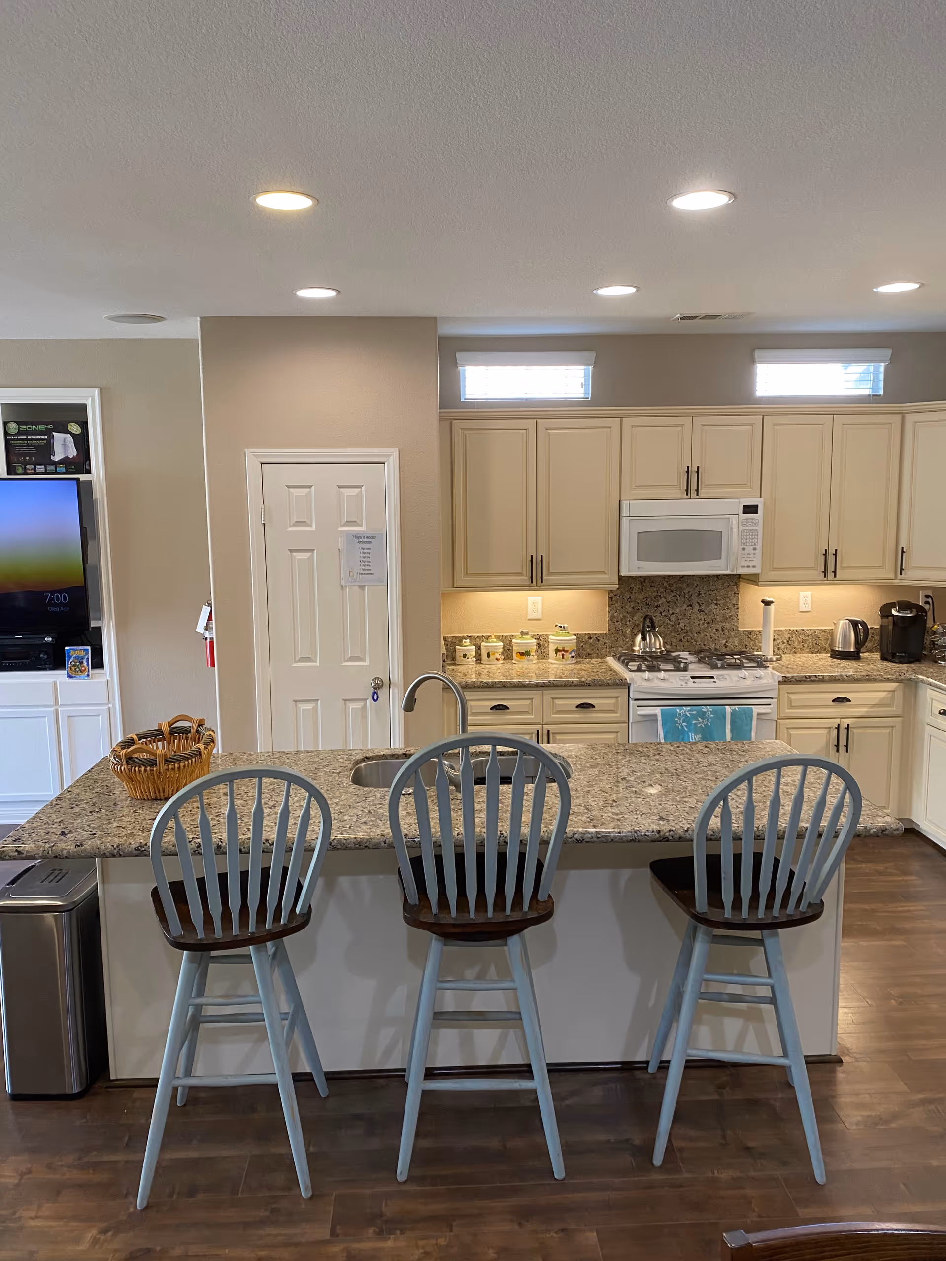 Spacious kitchen with granite island, three blue-gray bar stools, and modern appliances.