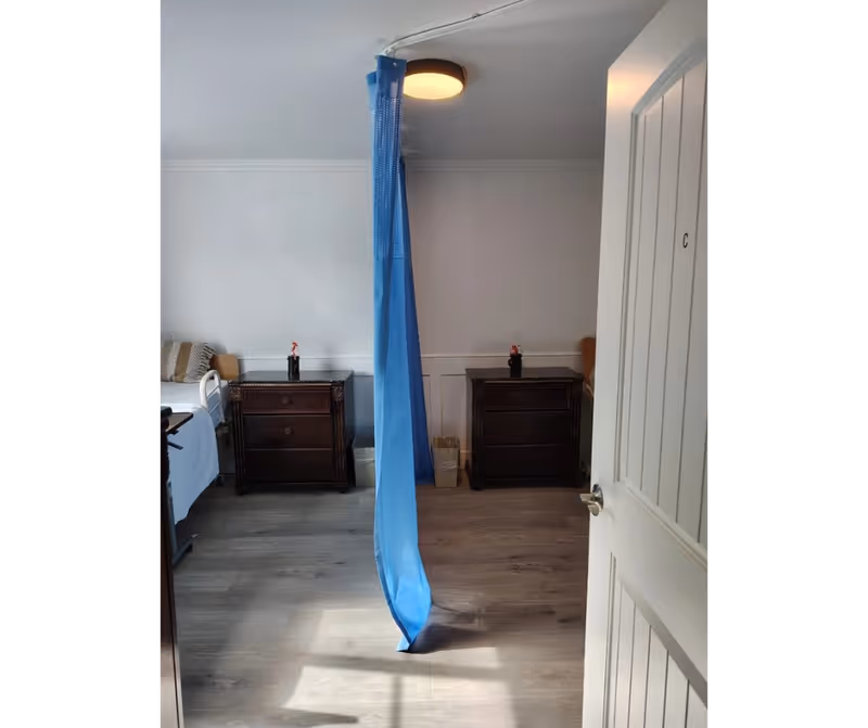 Two beds with dark bedside cabinets divided by a blue privacy curtain in a shared bedroom.