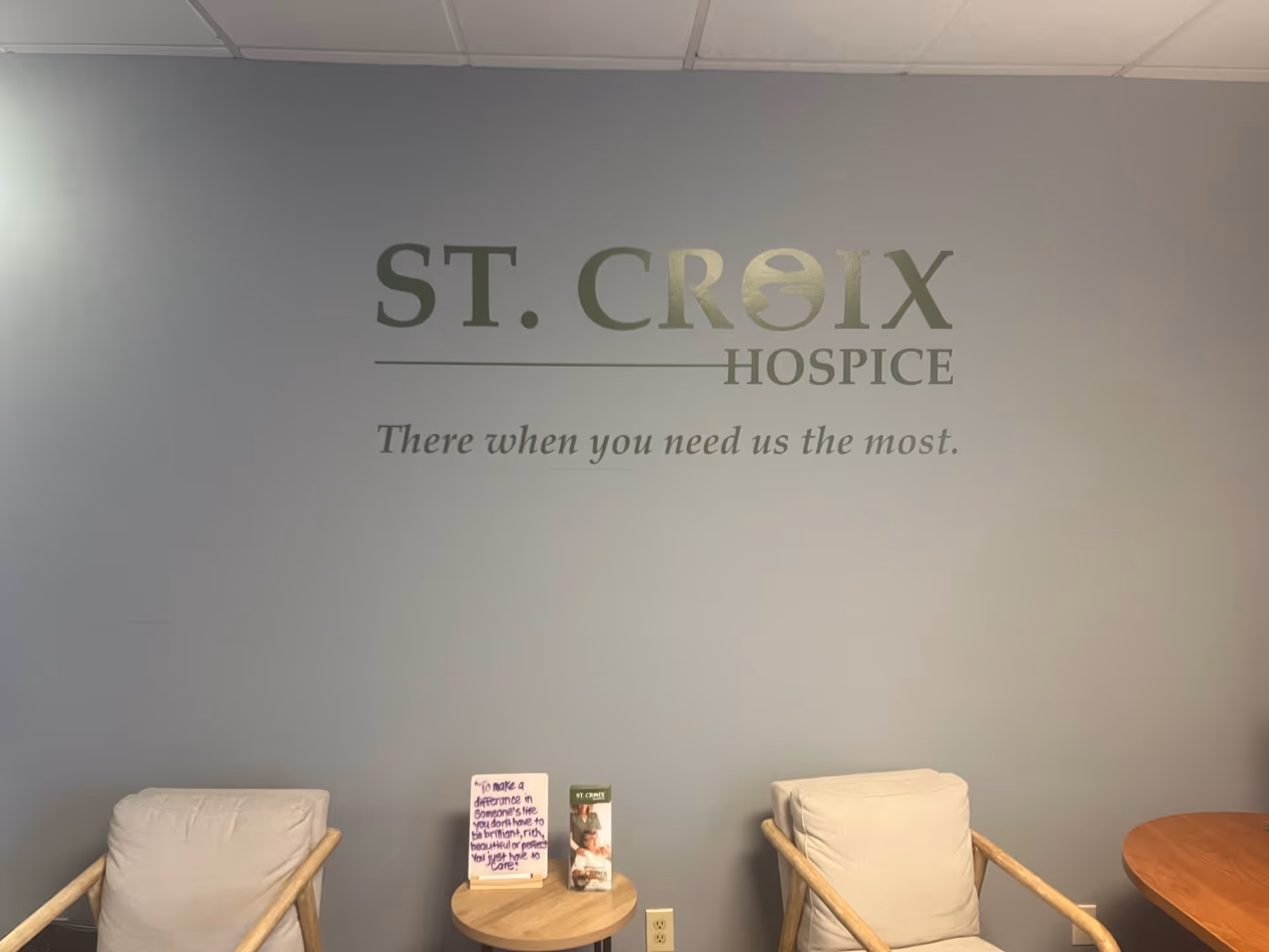 Interior lobby with ST. CROIX HOSPICE logo on a blue-gray wall and two cream chairs.