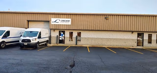 Exterior view of LINCARE facility with a parking lot and two white vans.