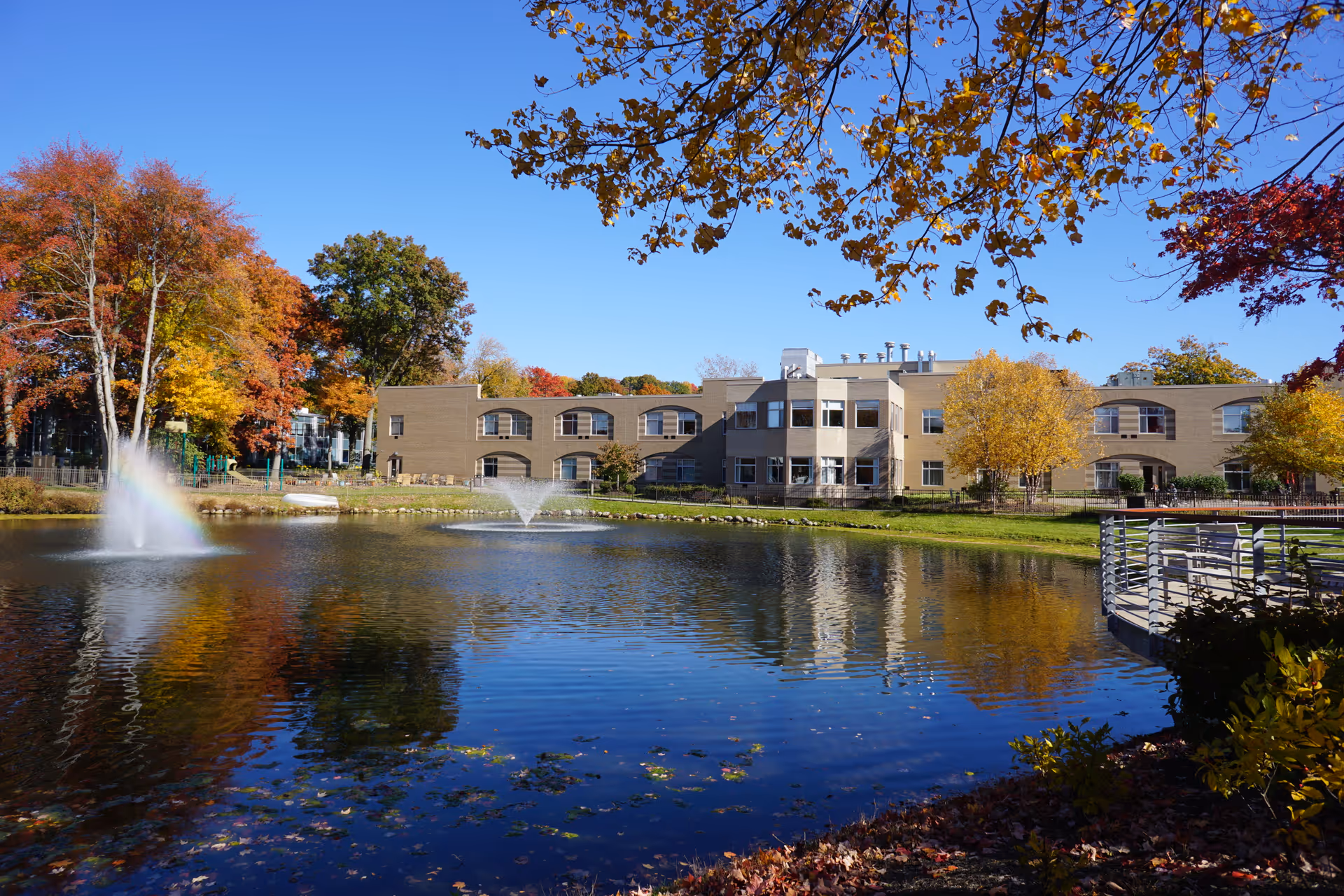 Exterior view of a Jewish Home Family senior living campus beside a pond and autumn trees.