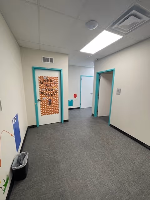 Interior hallway with teal door frames, ceiling tiles, and a trash can.