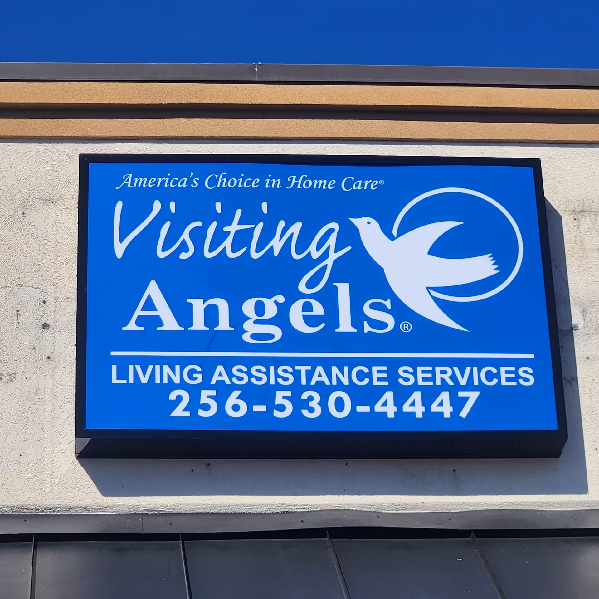 Blue Visiting Angels sign on building exterior with logo and contact number.