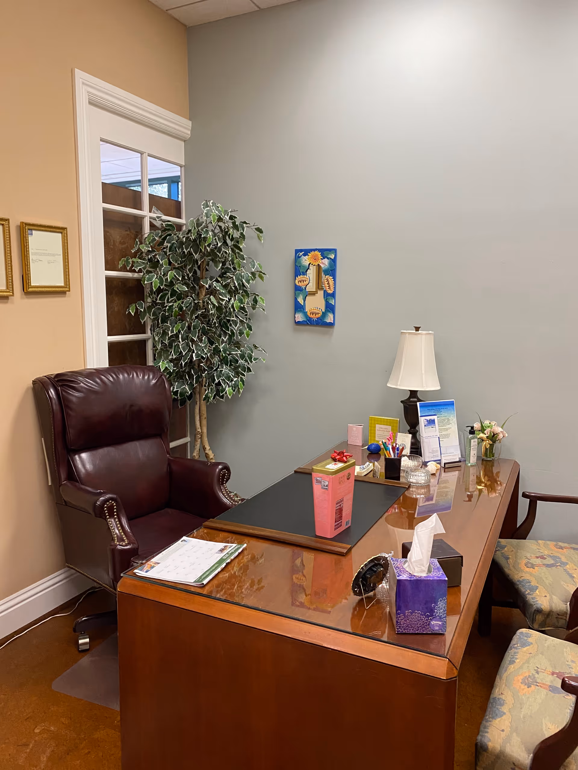 Wooden office desk with leather chair, lamp, plant, and decorative items in a quiet reception area.