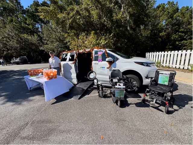 Outdoor mobility event with a van, wheelchairs, and tables with orange gift bags.
