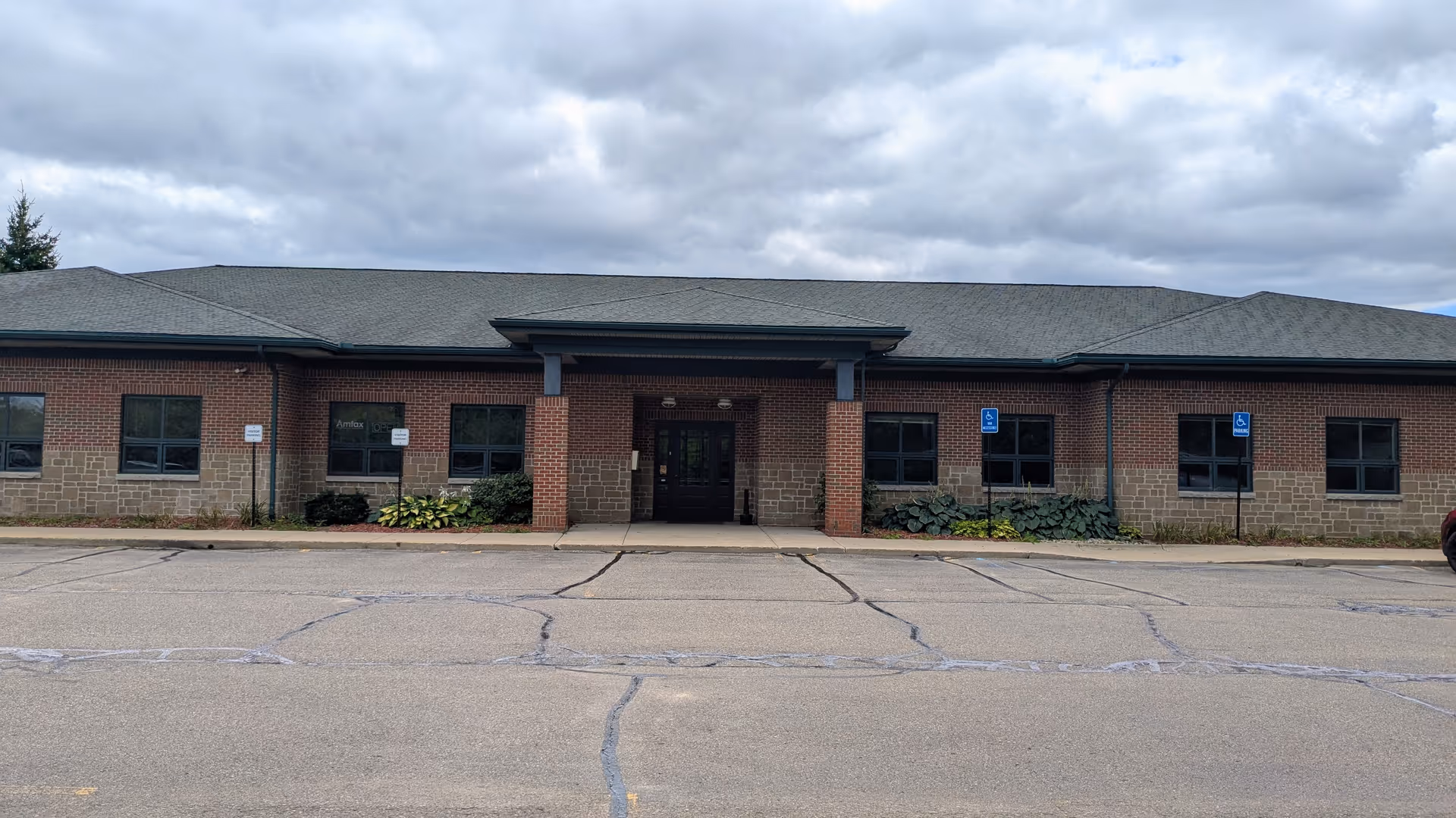 Front view of a single-story brick senior living facility entrance with a parking lot.