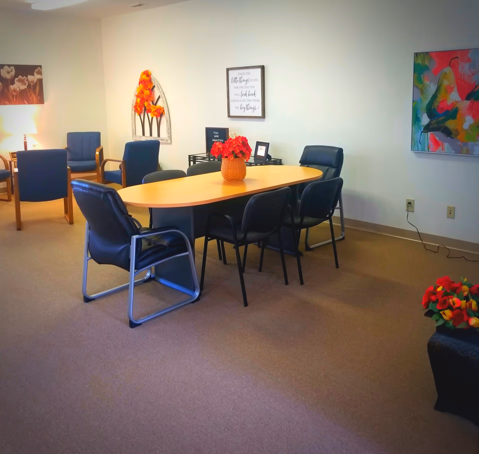 Bright senior living dining area with oval table, blue chairs, and colorful wall art.