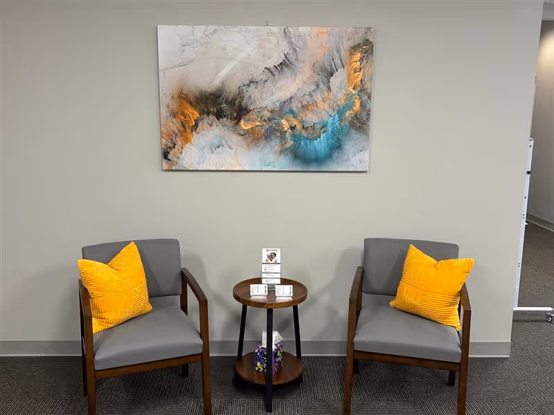 Two gray chairs with yellow cushions flank a small round table in a neutral lobby.