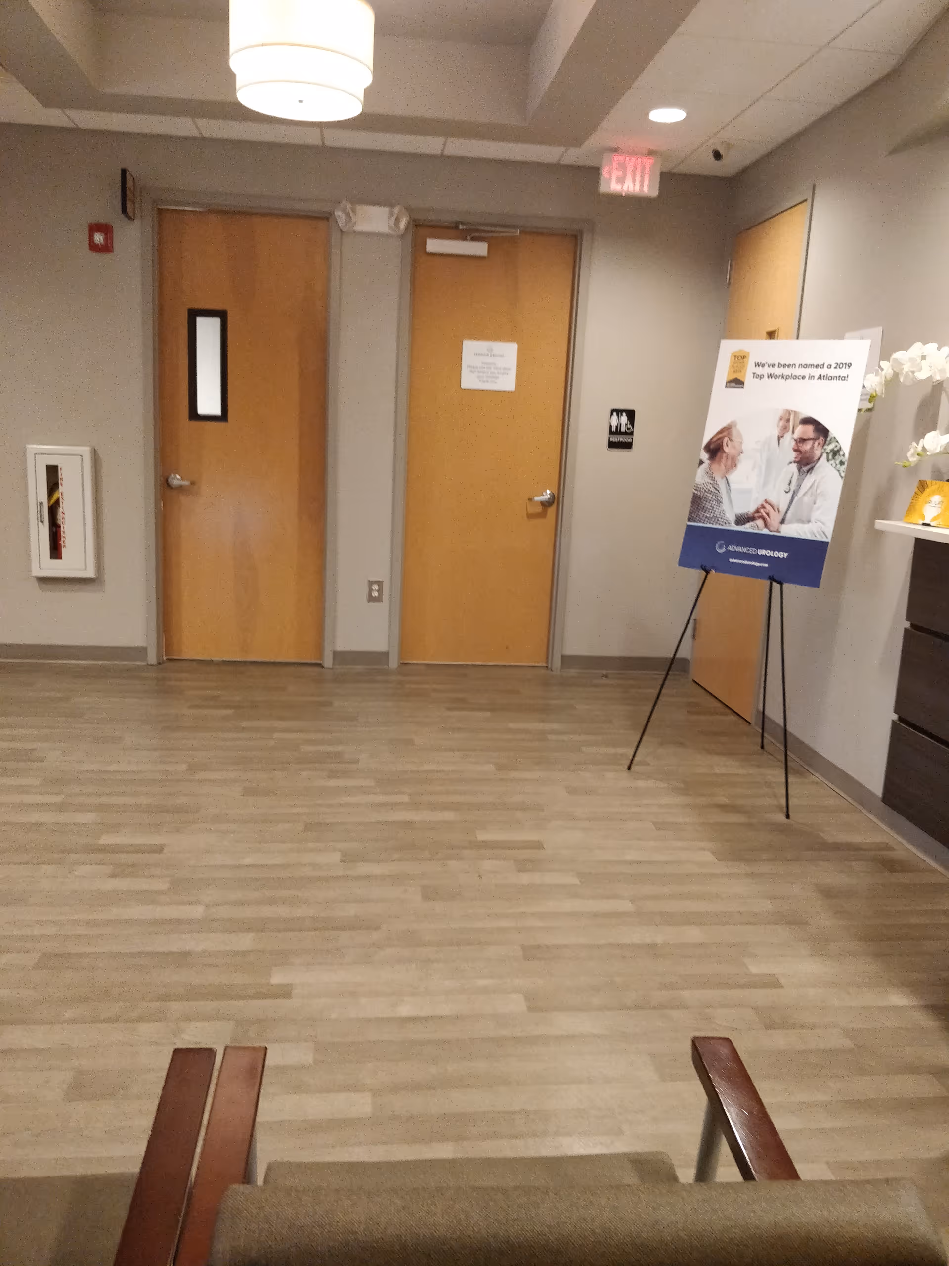 Wide hallway with wooden doors, exit sign, poster board, and bench in a modern interior.