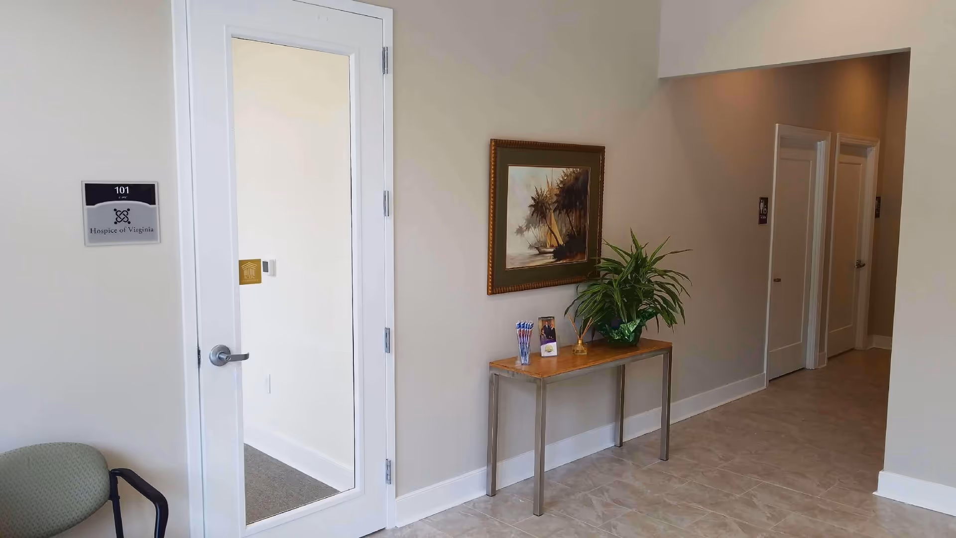 Hallway interior of Hospice of Virginia with doorway, framed painting, potted plant, and console table.