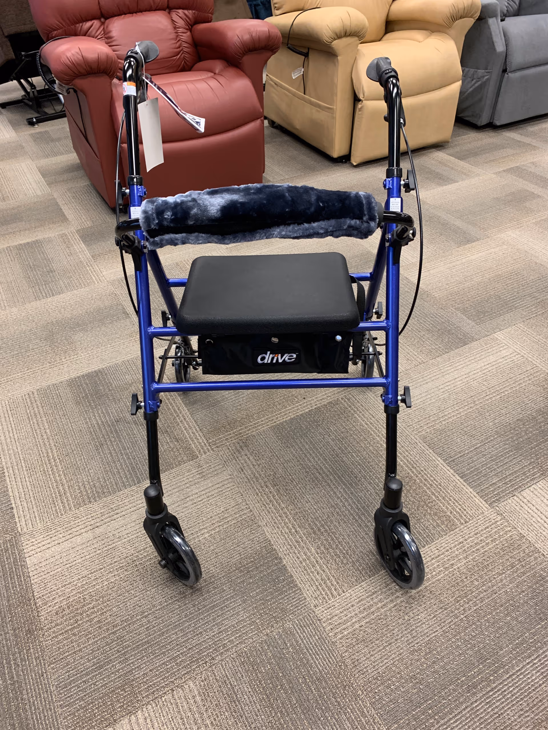 Blue wheeled walker with padded seat displayed among recliners.