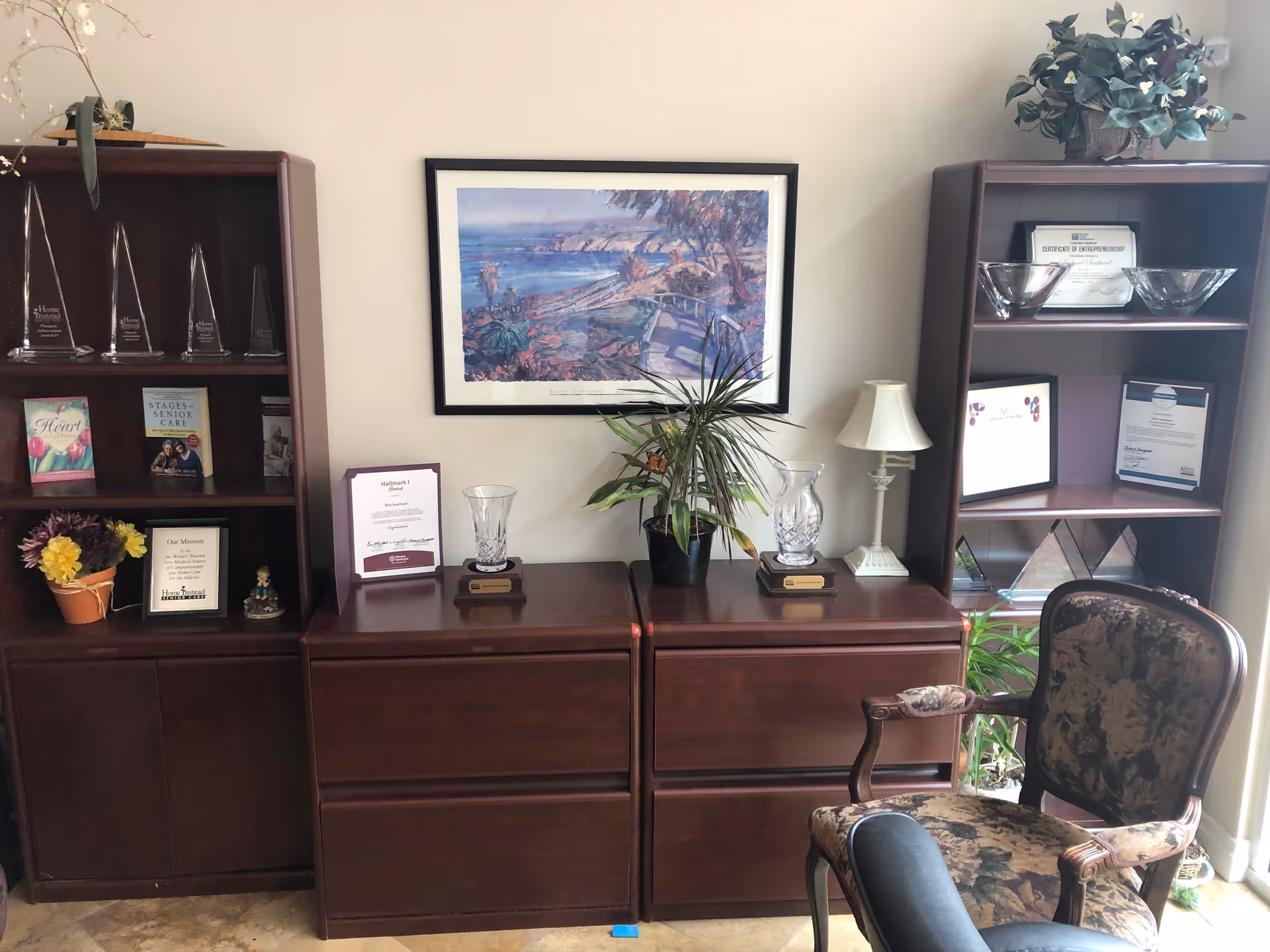 Dark wood cabinets flank a central cabinet with awards, a painting, and potted plants.