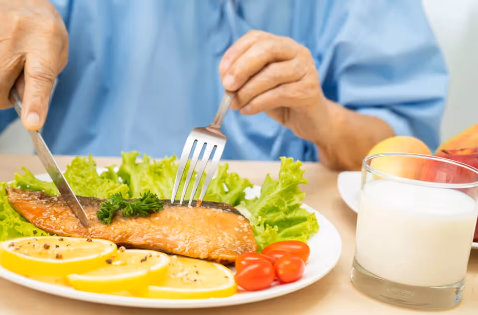 A plate with salmon, lemon, greens, tomatoes, and a glass of milk on a table.