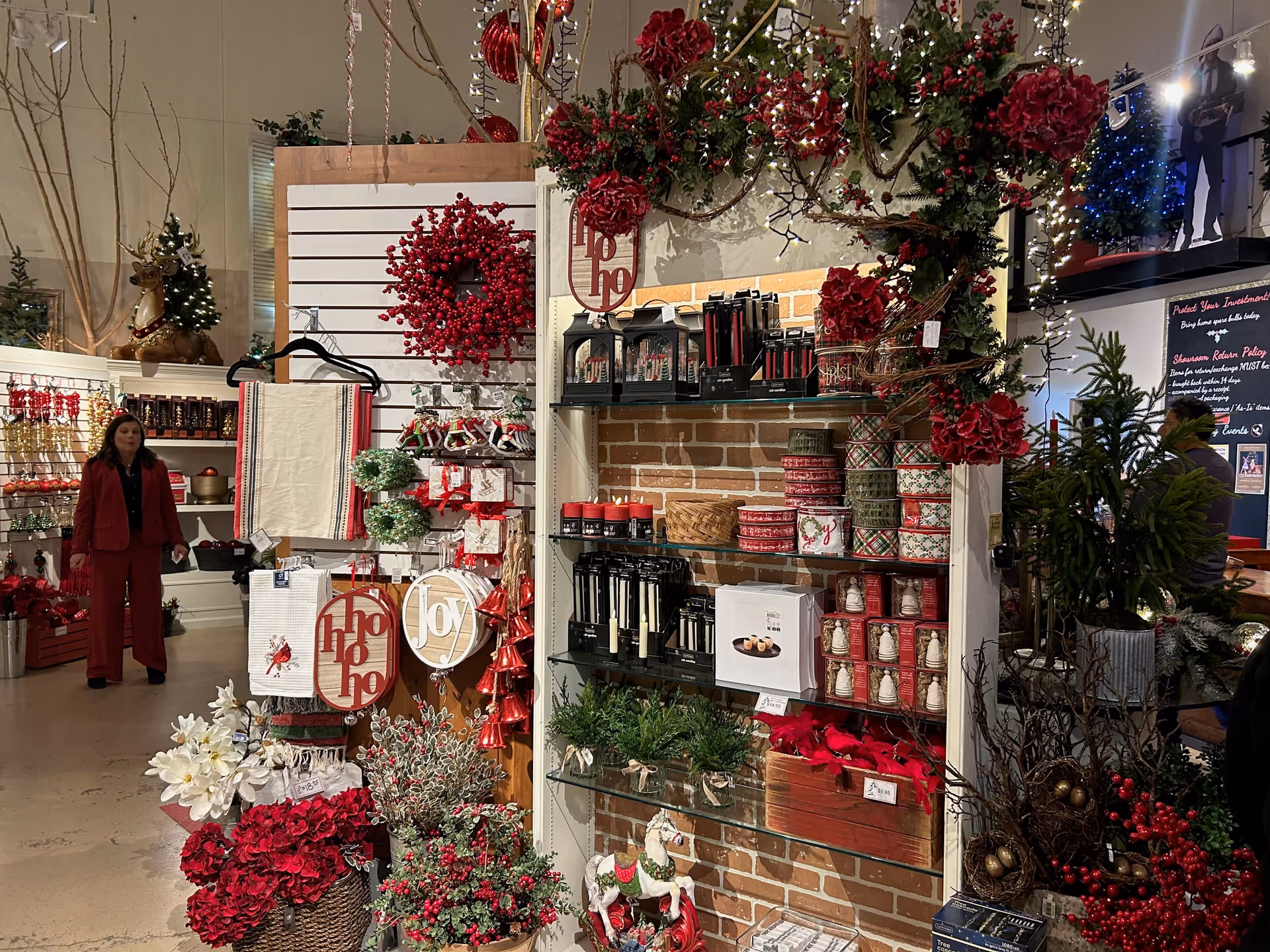A person in red stands near shelves of festive holiday decorations indoors.