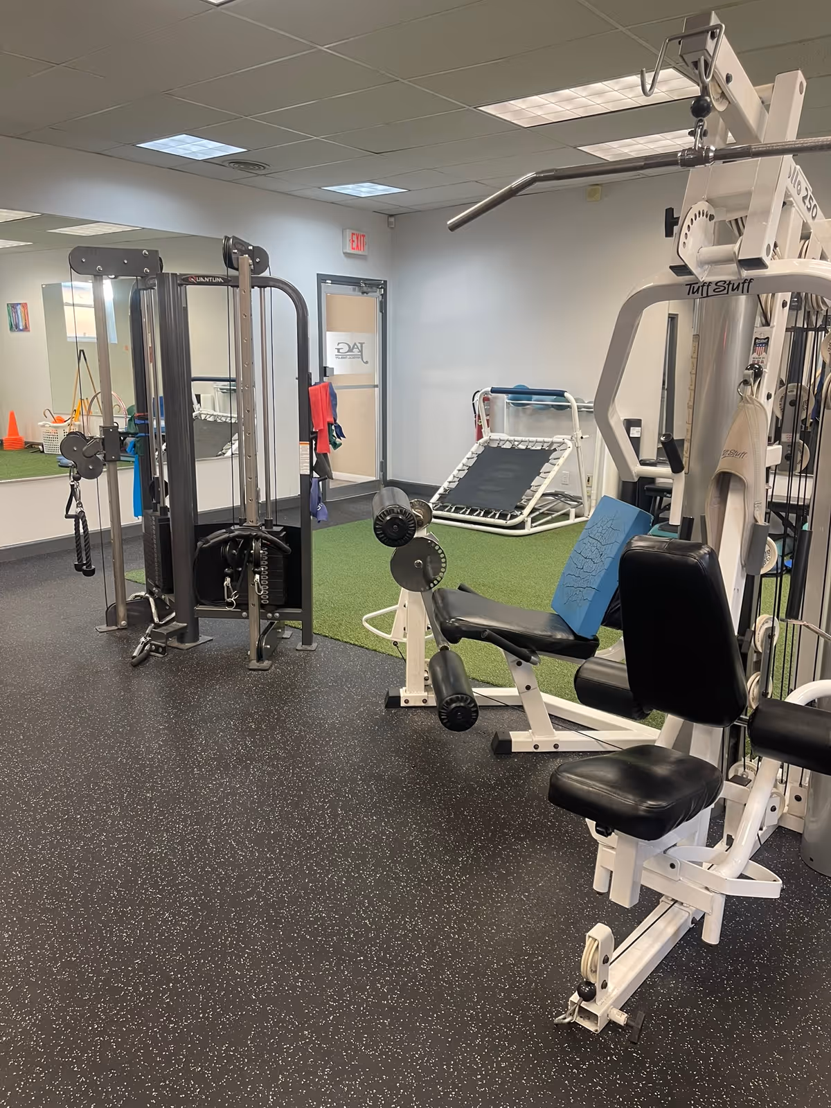 Interior senior living fitness room with weight machines, benches, and cardio equipment.
