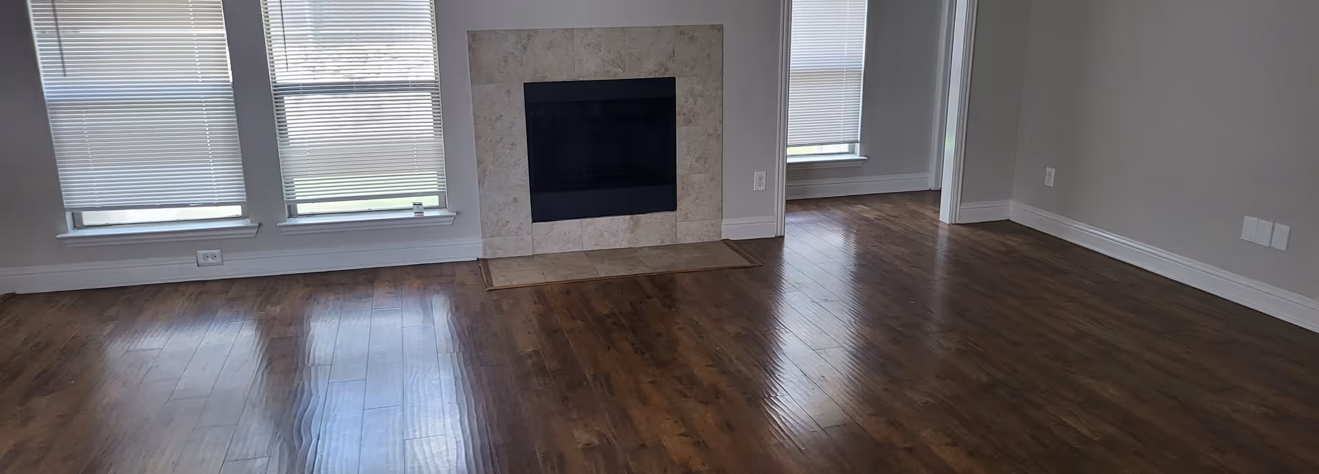 Spacious living room in a senior facility with hardwood floors, windows, and a fireplace.