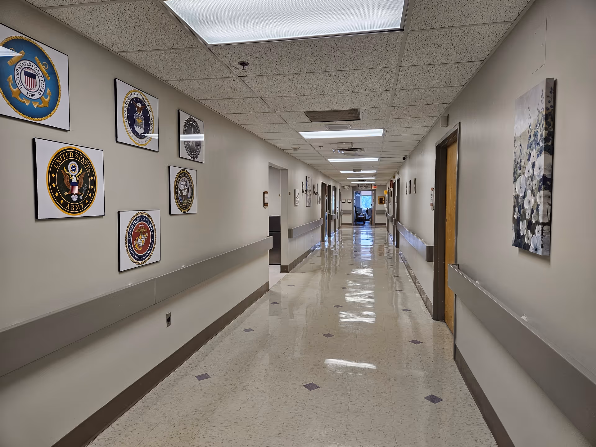 Long hospital hallway with framed insignias on the left and artwork on the right.
