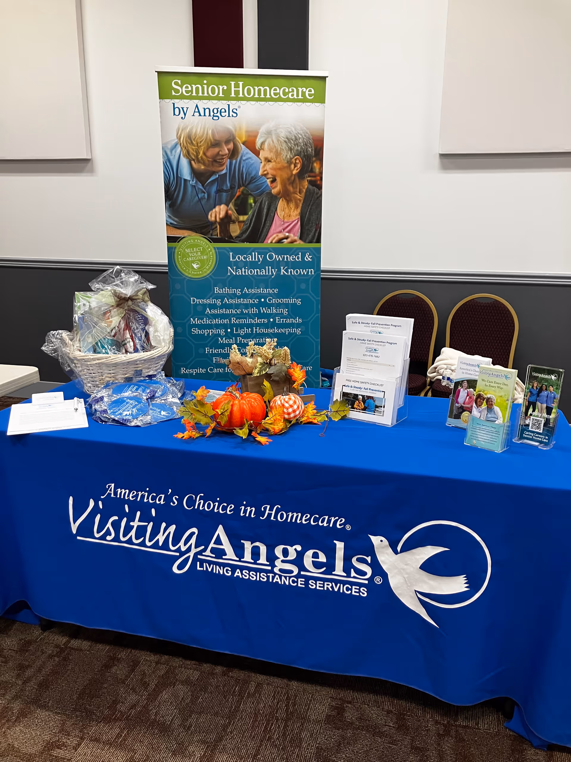 Promotional display table with Visiting Angels banner and brochures in a conference room.