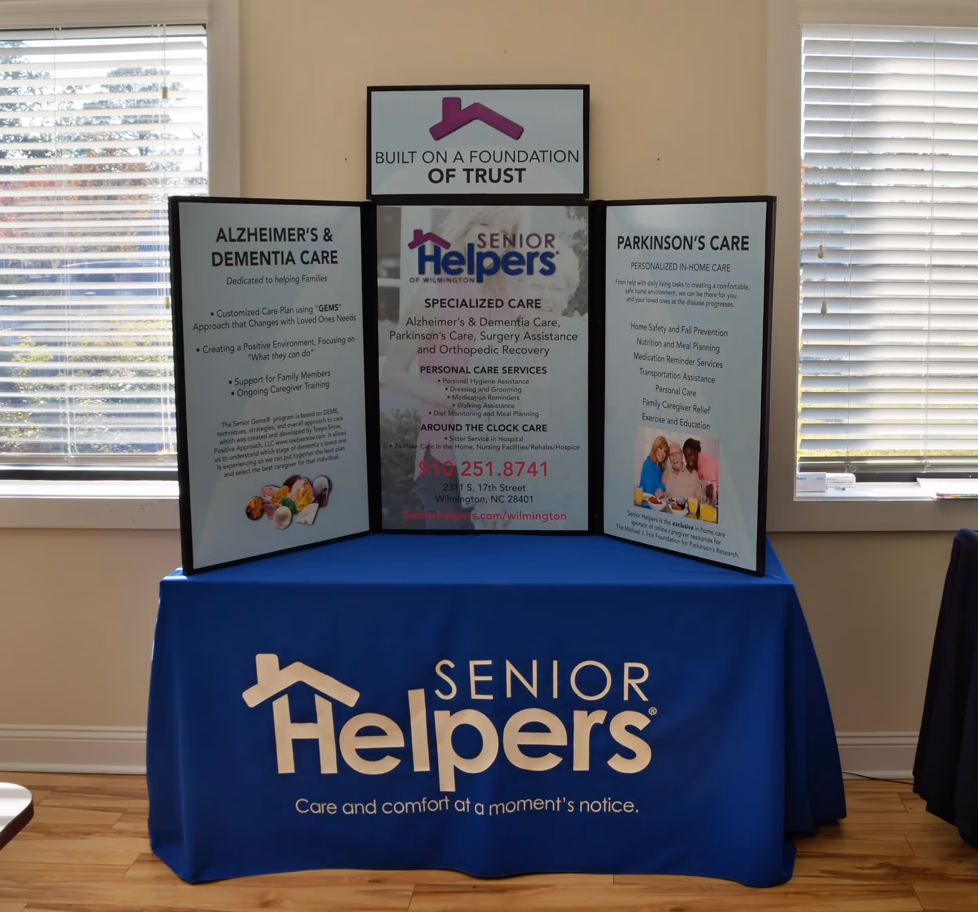 Three-panel information display on a blue table promoting Senior Helpers inside a bright room.
