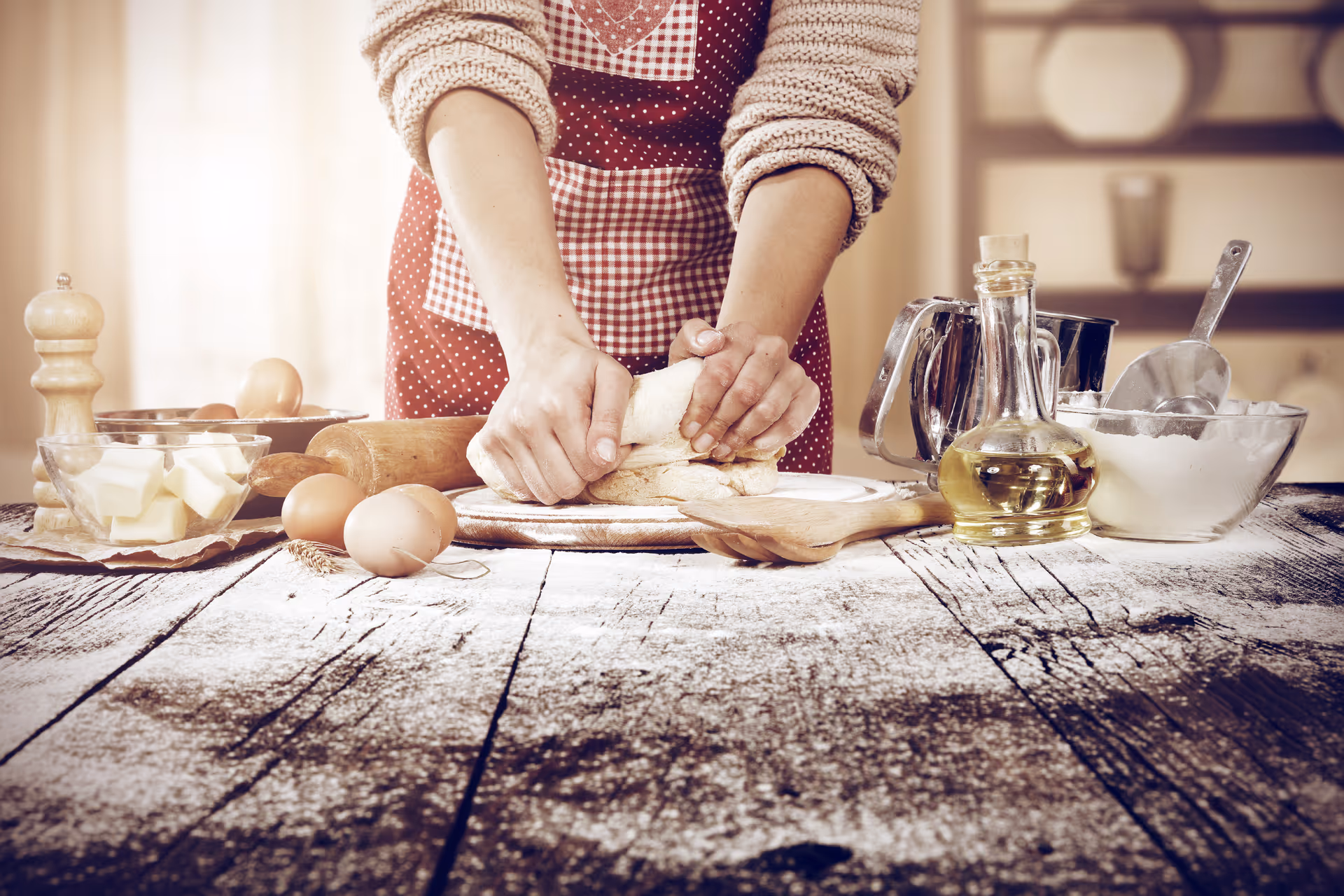 Hands kneading dough on a rustic kitchen table with eggs, butter, and oil.
