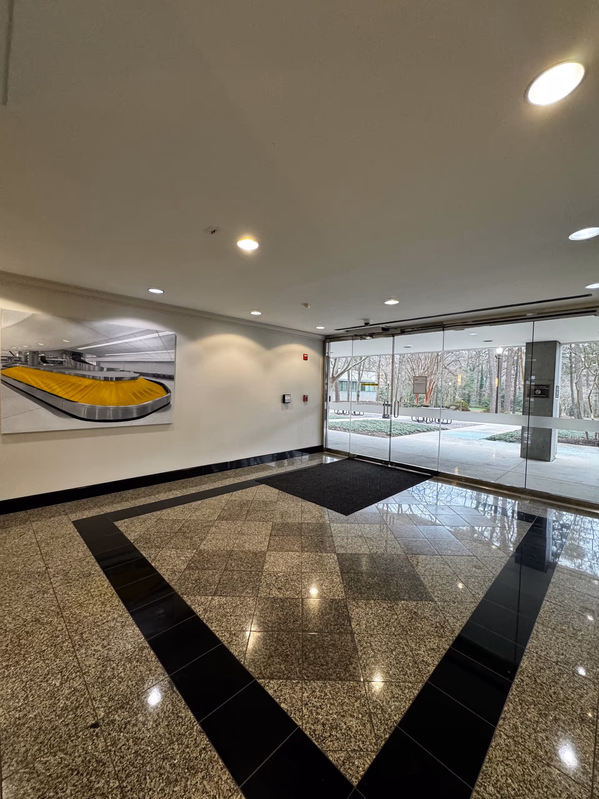 Bright modern lobby with glass doors, tiled floor, and wall artwork.