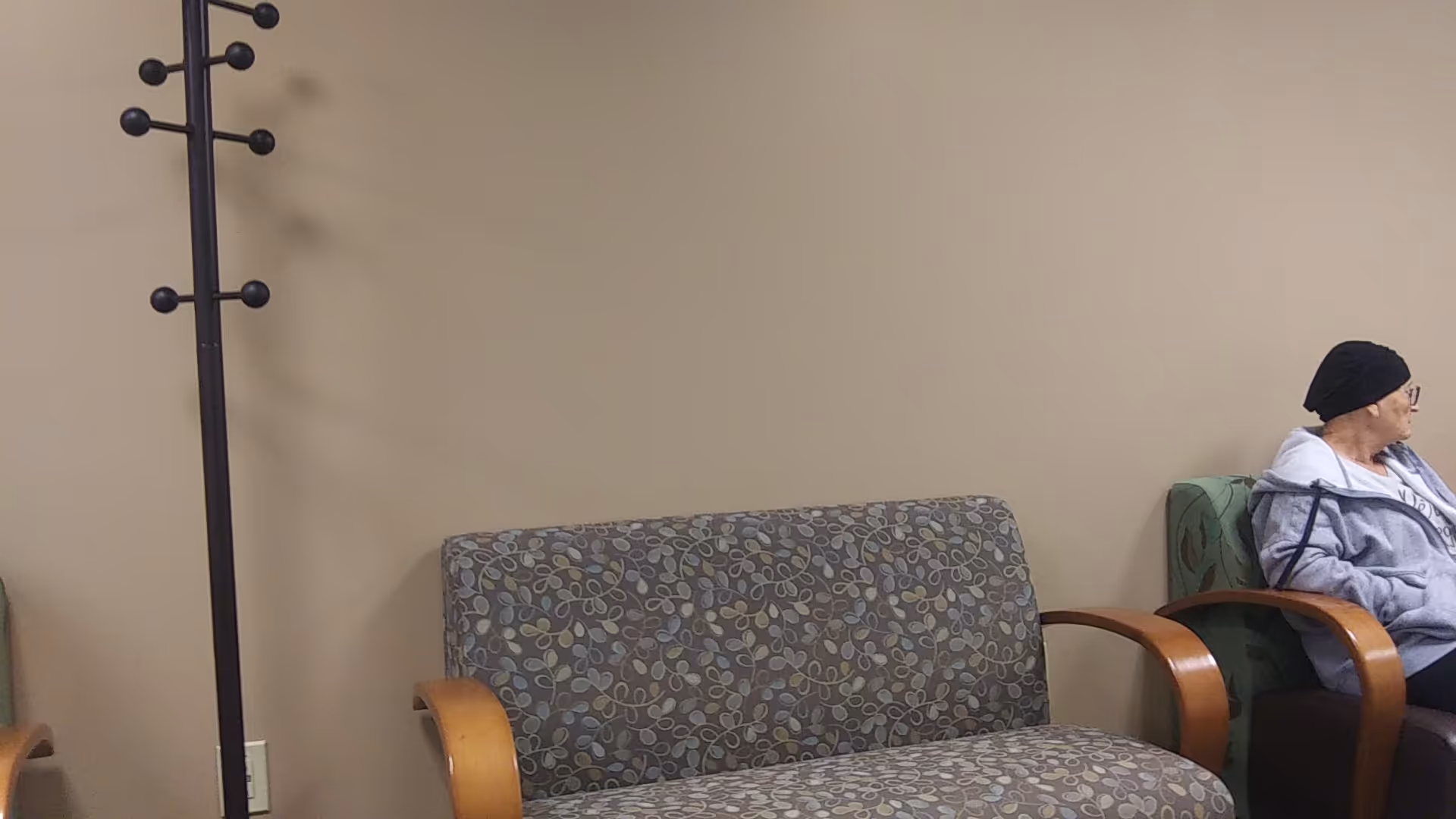 A person sits in a beige lounge area with patterned sofa and wooden armrests.