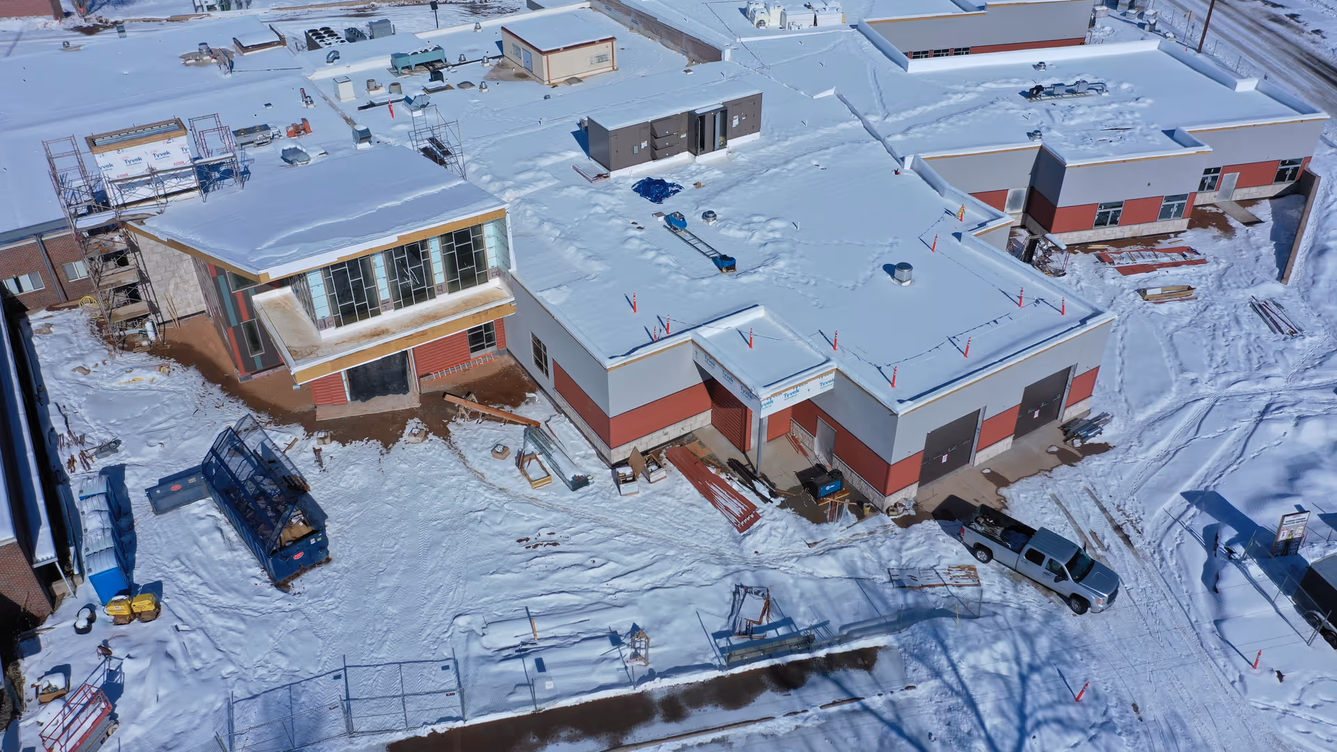 An aerial view of a snow-covered health facility complex with red-gray buildings.