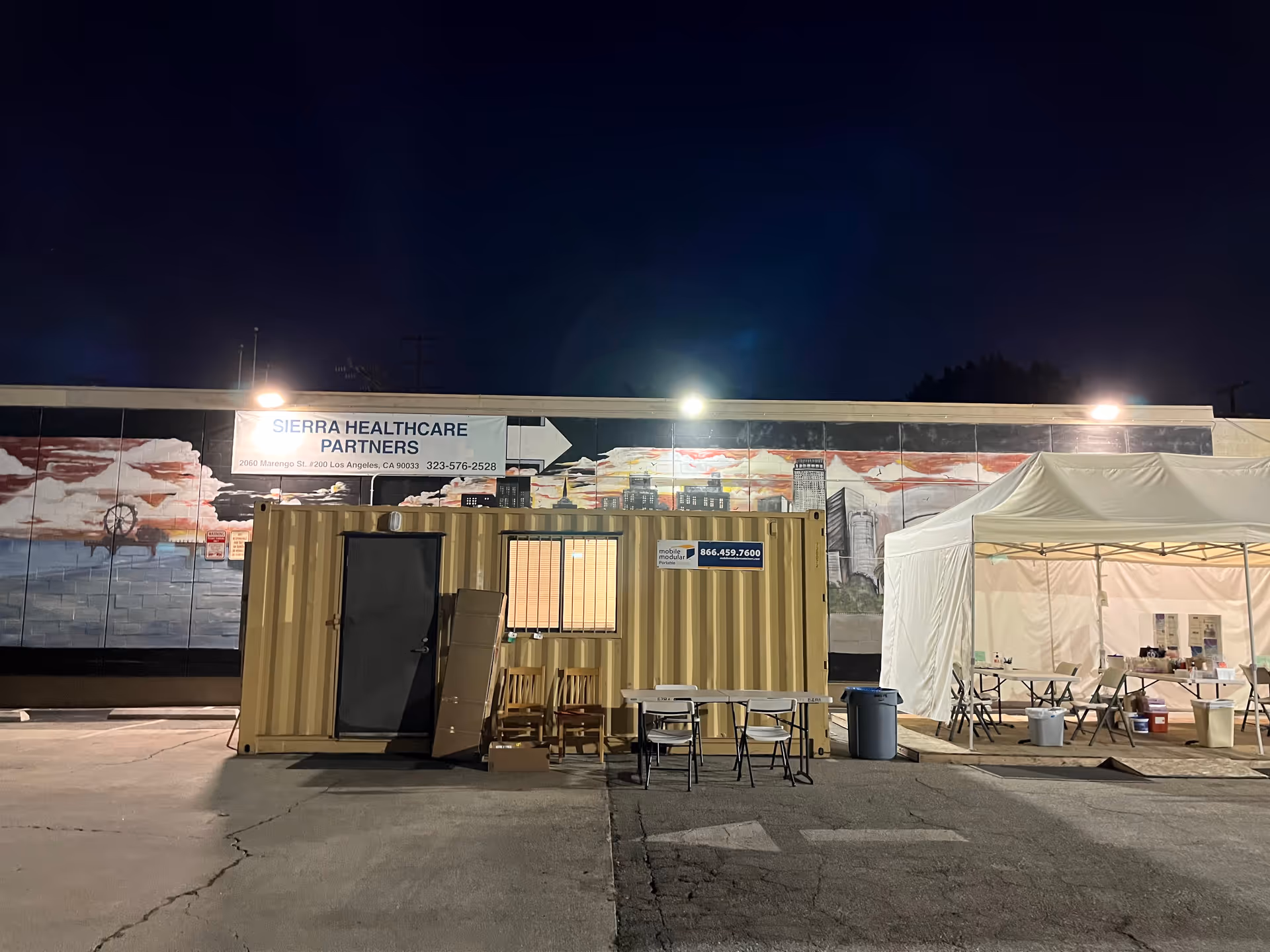Night exterior view of Sierra Healthcare Partners facility with a shipping container and white event tent.