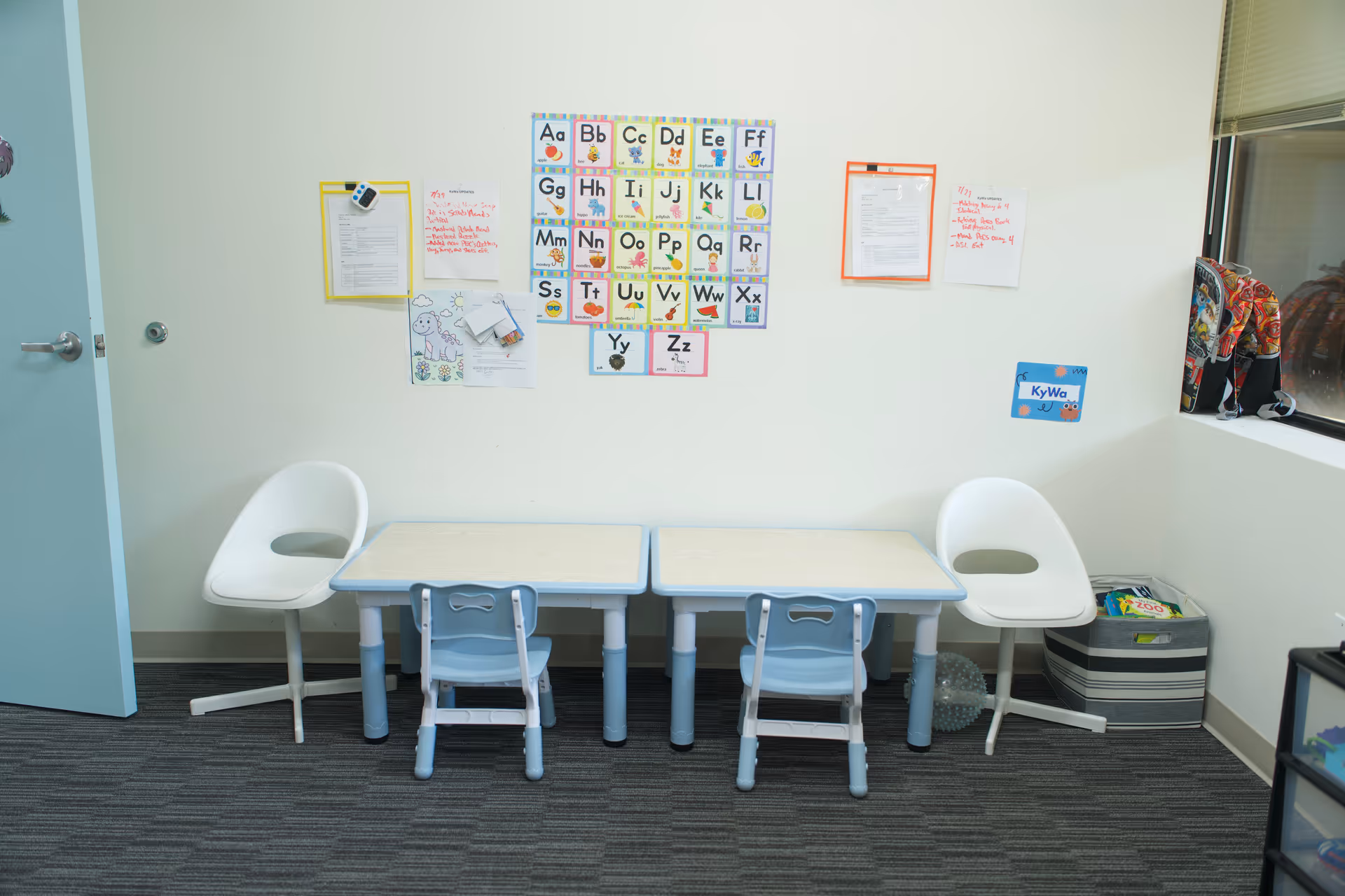 Child-sized tables and chairs arranged in a small classroom area with alphabet posters.