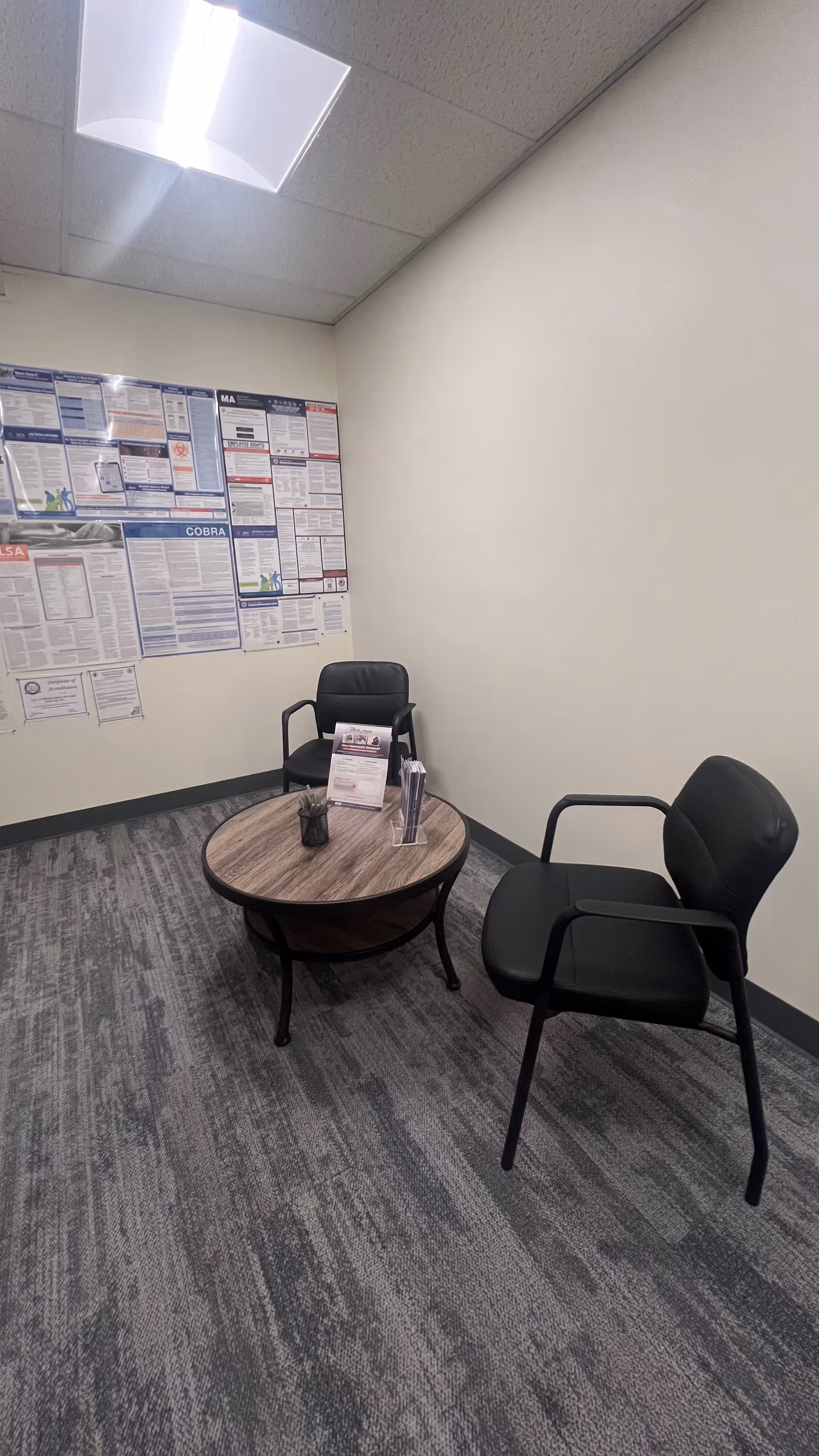 Small indoor waiting area with two black chairs around a round wooden table.