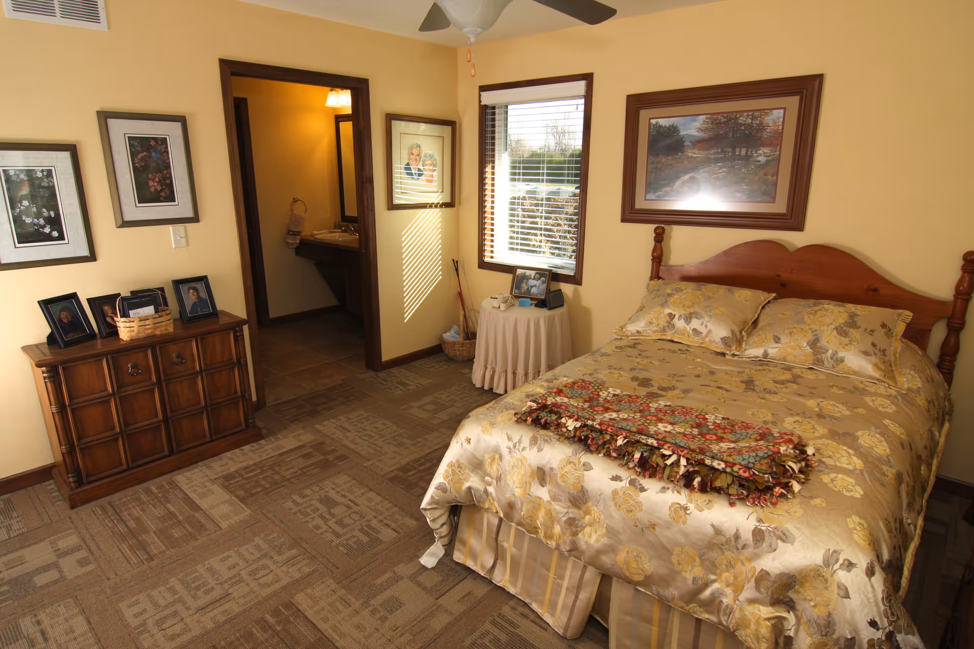 Cozy bedroom featuring a wooden bed, dresser with photos, framed art, and adjacent bathroom doorway.