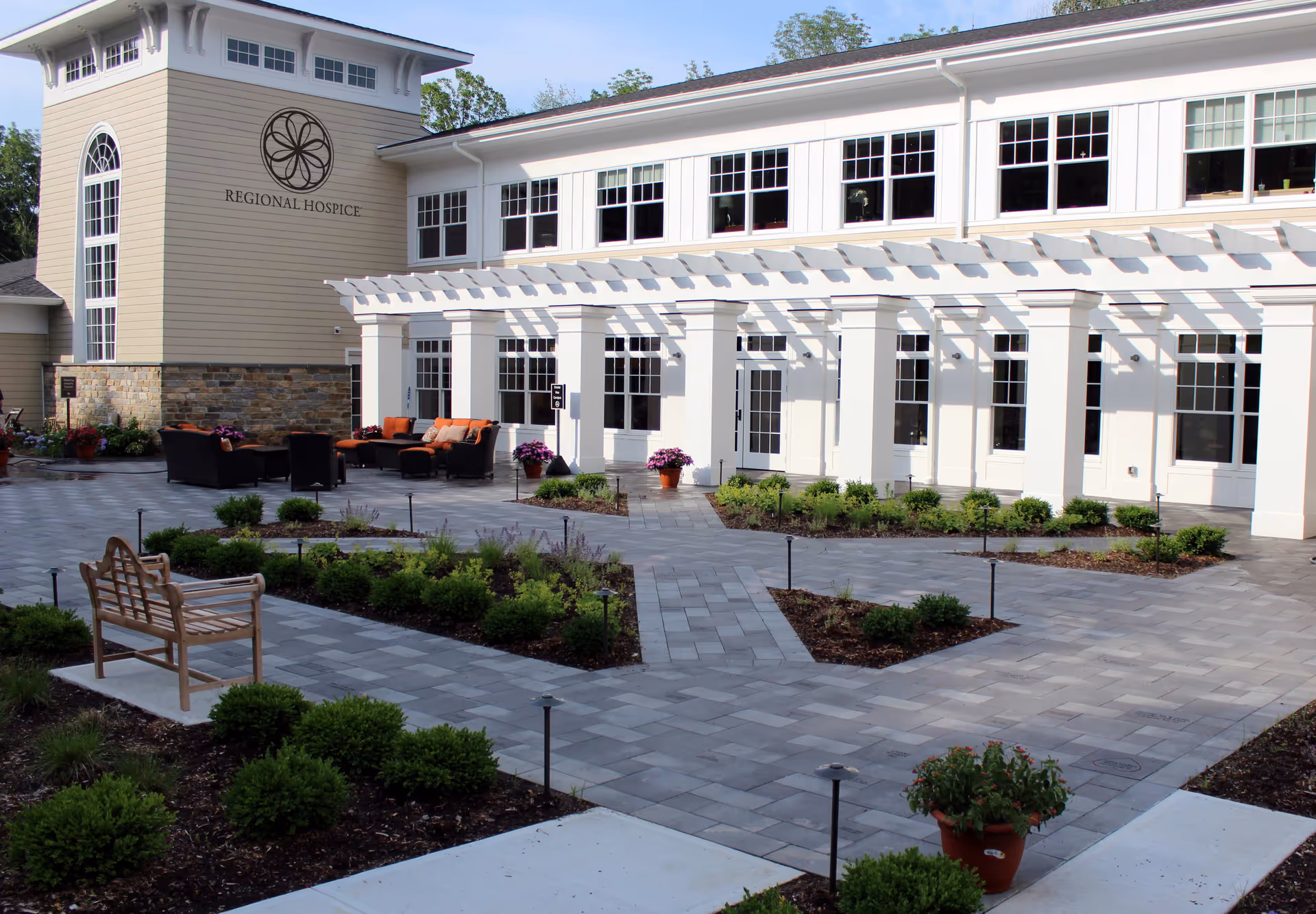 Exterior view of Regional Hospice building with a paved courtyard and outdoor seating.