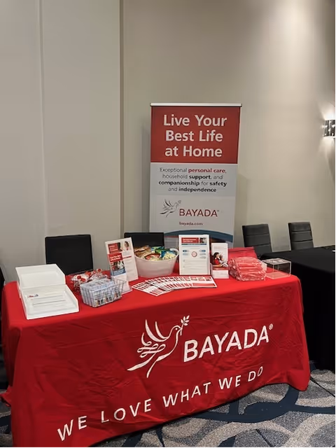 Indoor conference display table with BAYADA banner and brochures on red tablecloth.