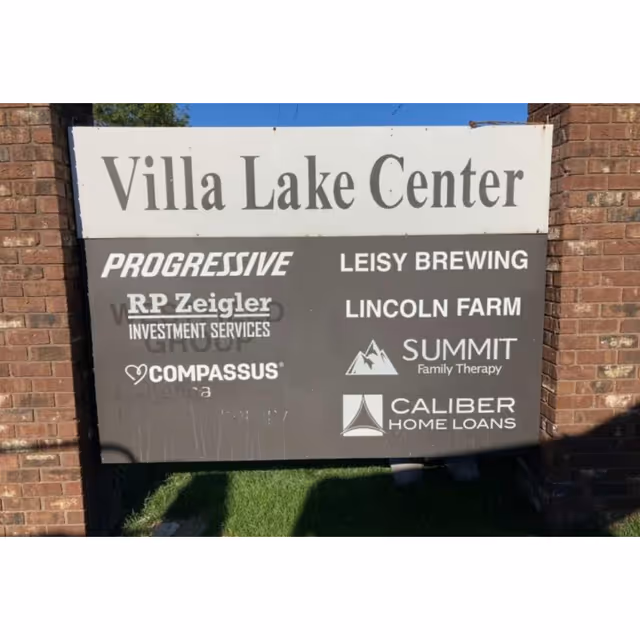Outdoor signboard on a brick wall displaying Villa Lake Center and sponsor logos