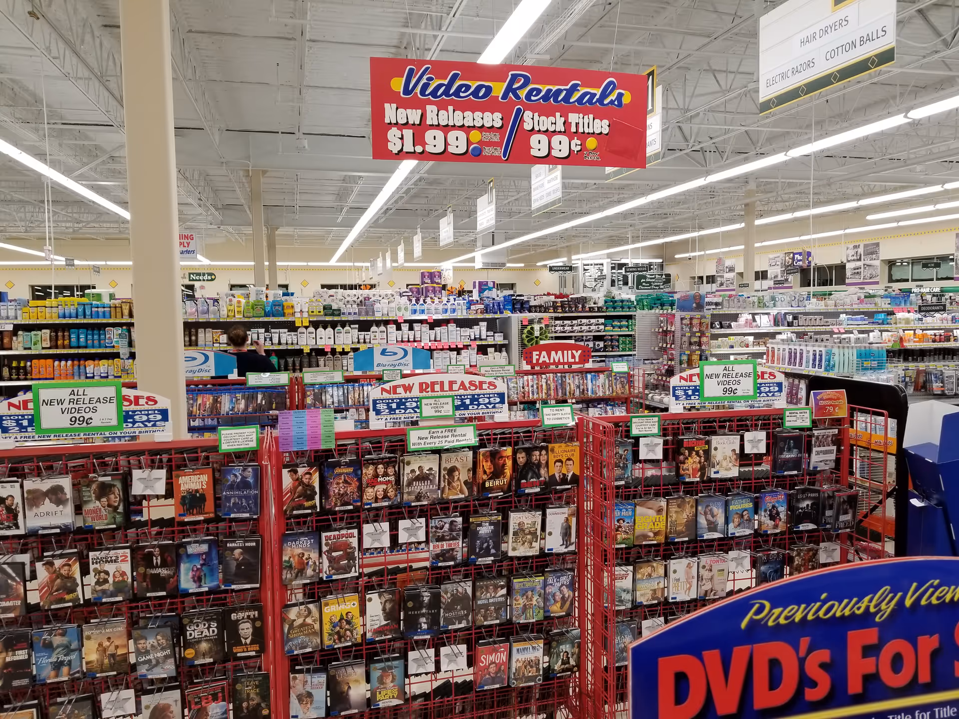 Inside Discount Drug Mart, DVD racks and magazines line bright store aisles under lights.