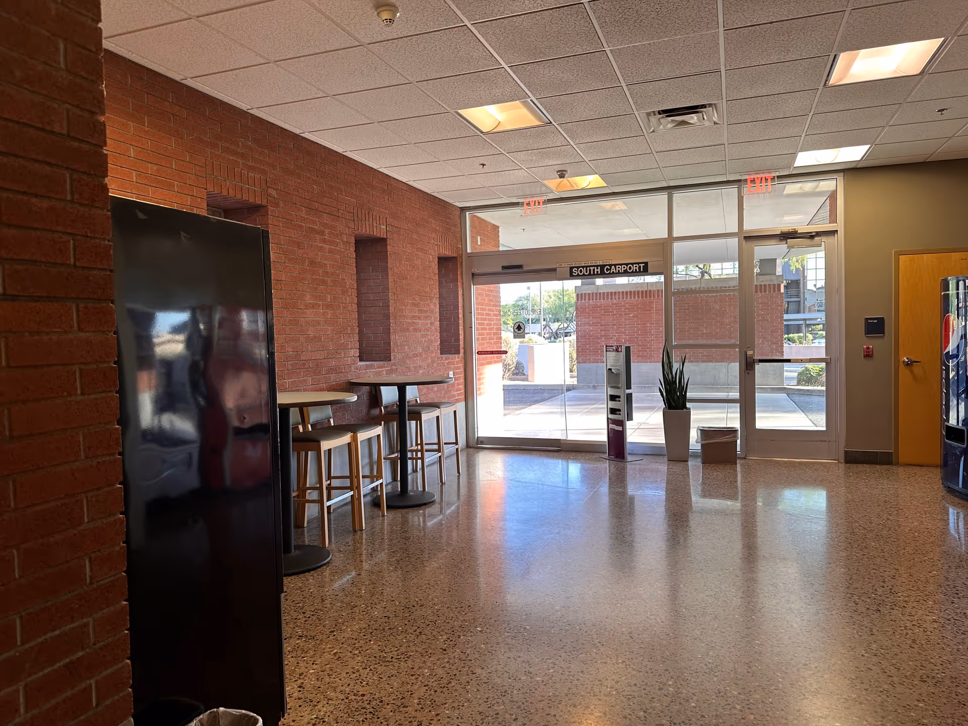 Hospital lobby entrance with brick walls, glass doors, and small tables and stools.